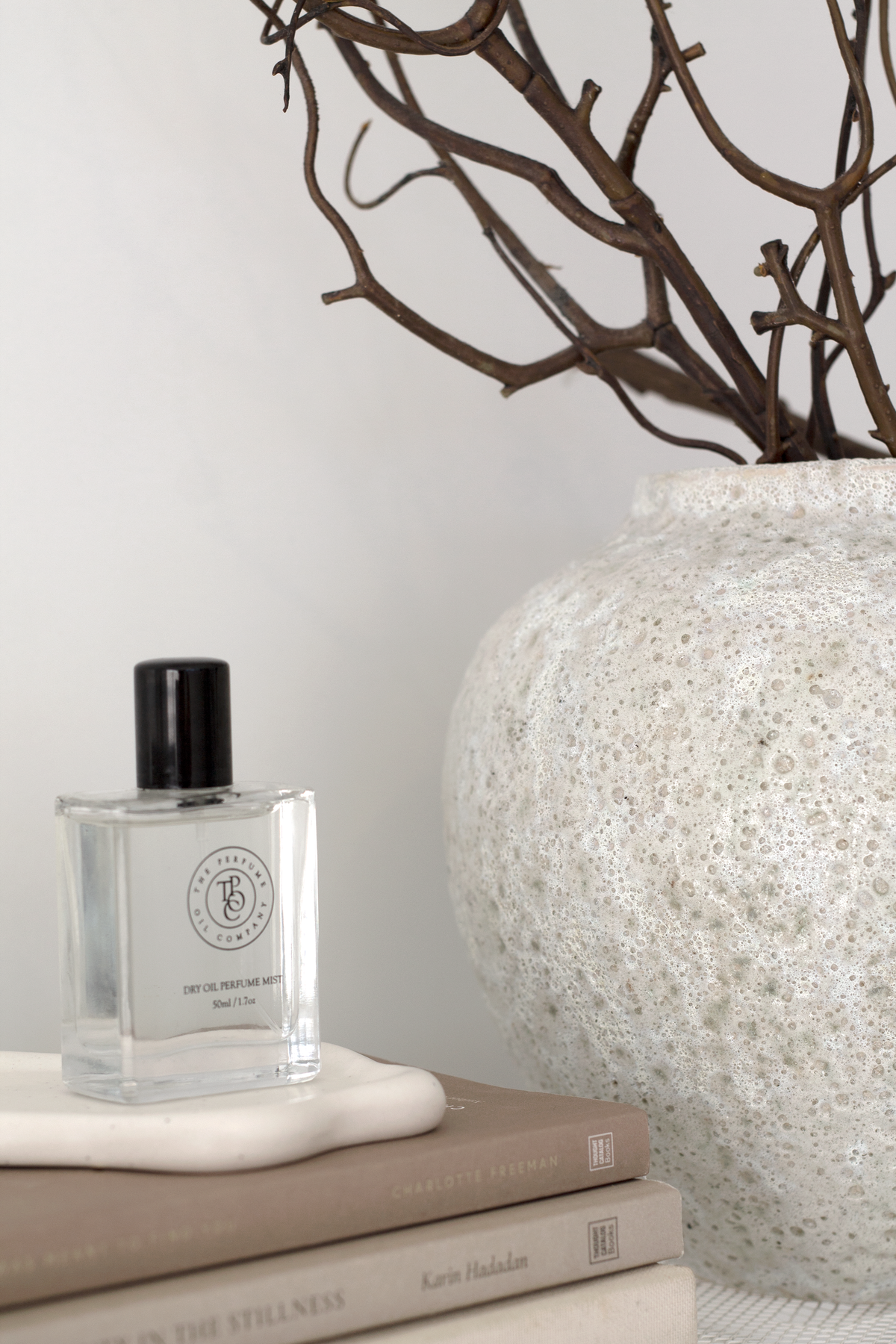 Short Seafoam vase of branches on a shelf beside a fragrance bottle resting on books