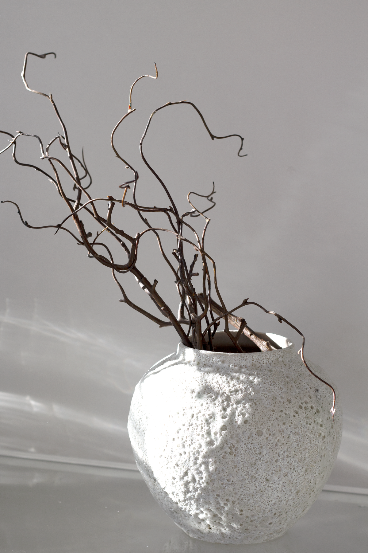 Short Seafoam vase holding curly willow branches against a soft grey backdrop