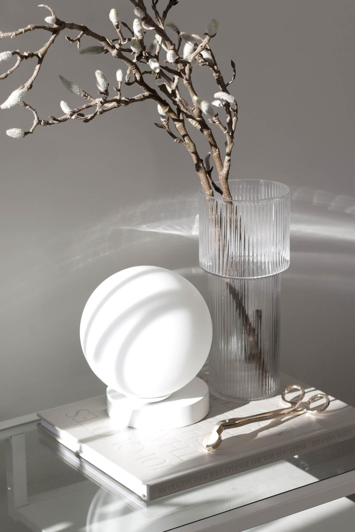 Yuri Table Lamp on stacked books beside a ribbed glass vase of magnolia branches