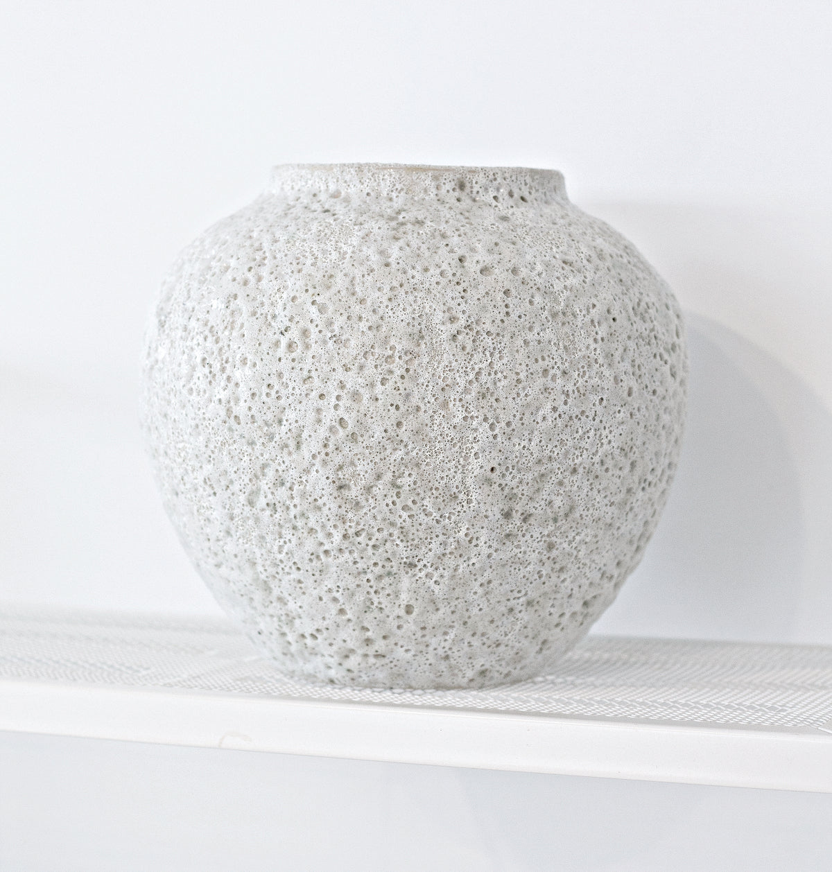 Short Seafoam vase shown empty on a white shelf, side light picking out the pitted surface