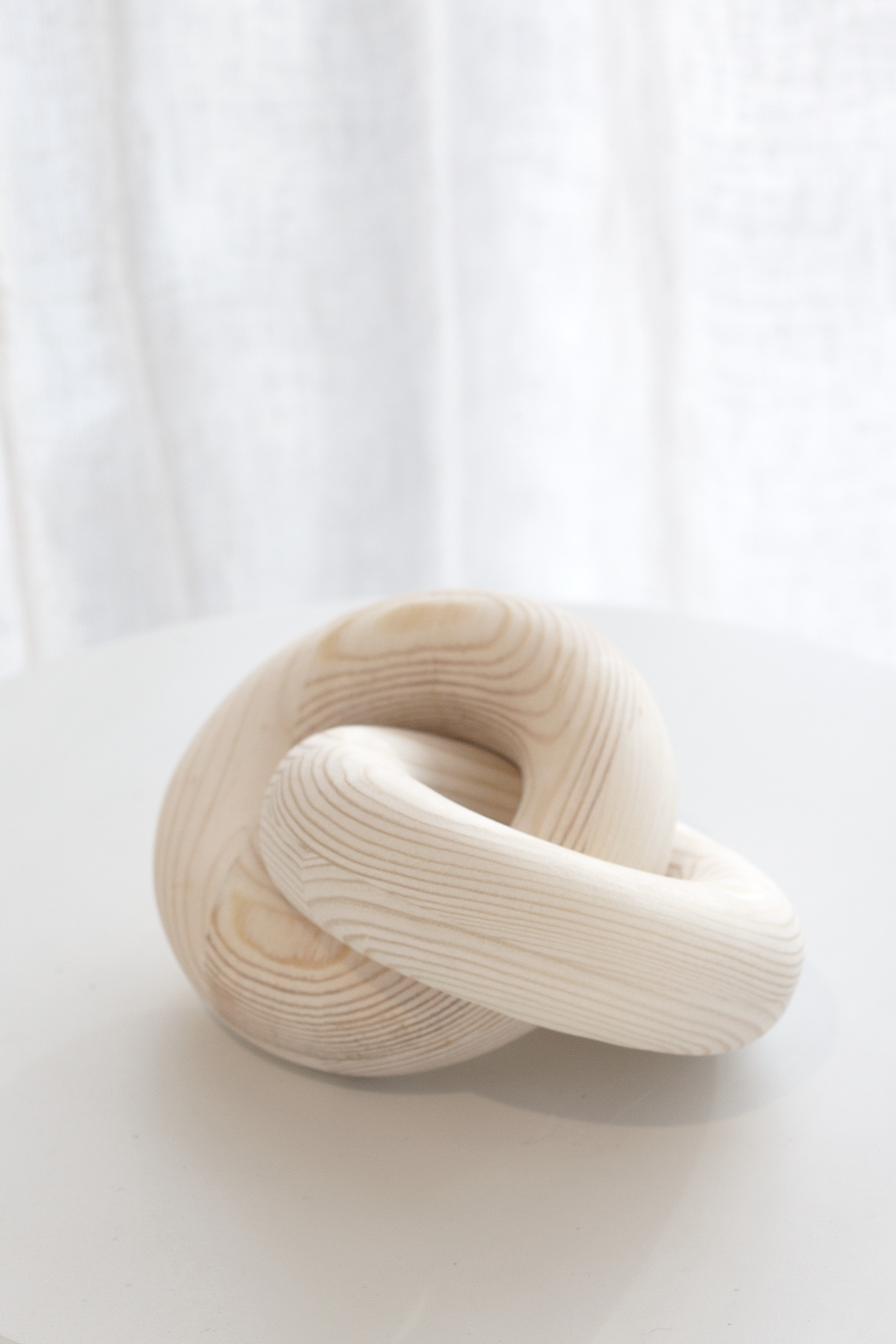 Natural wood knot sculpture on a white table with a sheer curtain behind