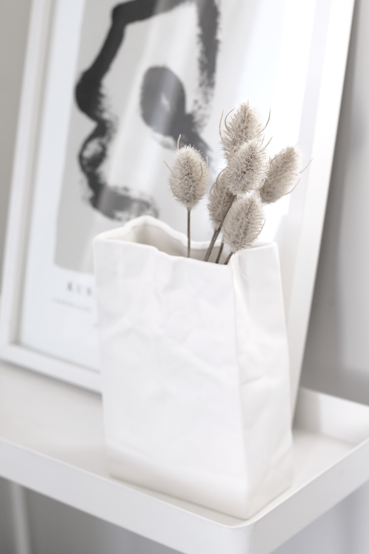 Faux bunny tails in a white paper-bag vase in front of abstract art