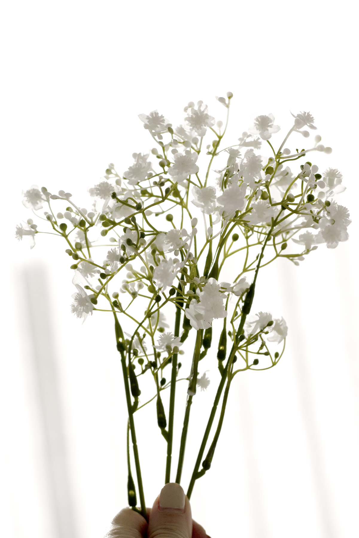 Faux gypsophila in a clear glass vase beside candles