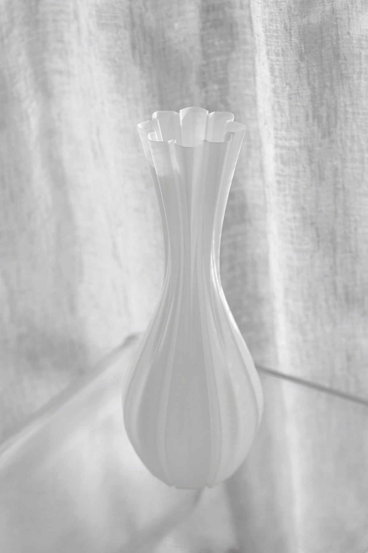 Soft high-key shot of the fluted white vase against a linen curtain, ribs catching faint light