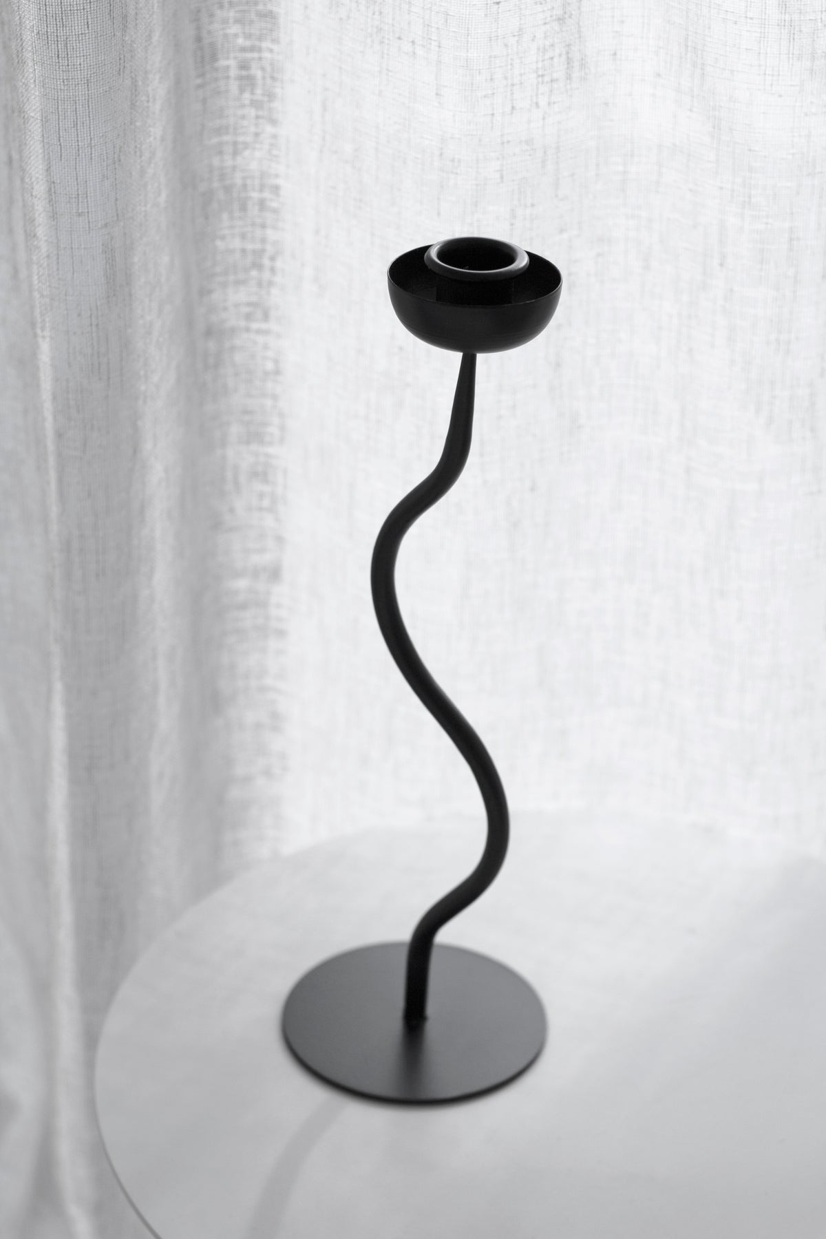 Aries candle holder standing empty on a round table against a linen curtain