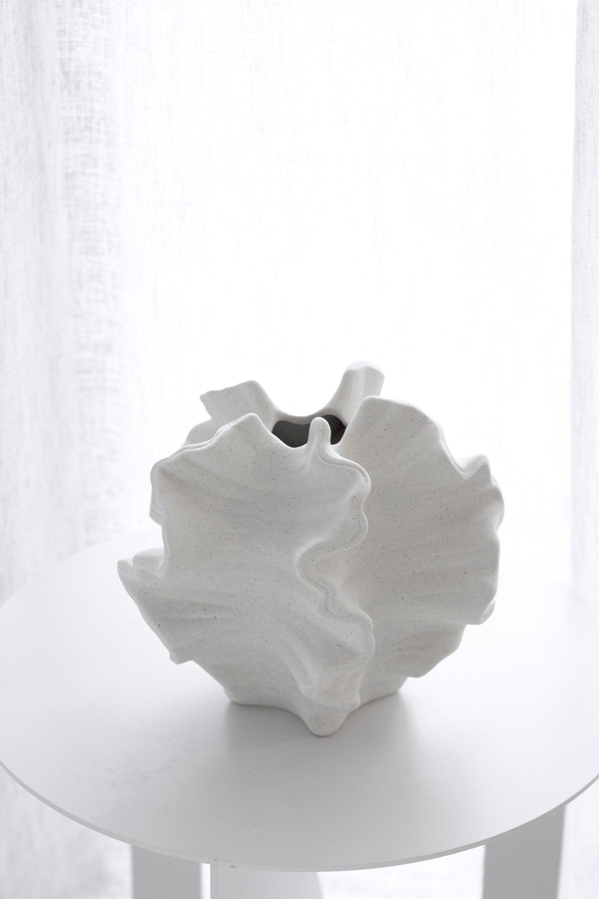 Coral vase on a round white side table with a sheer curtain behind