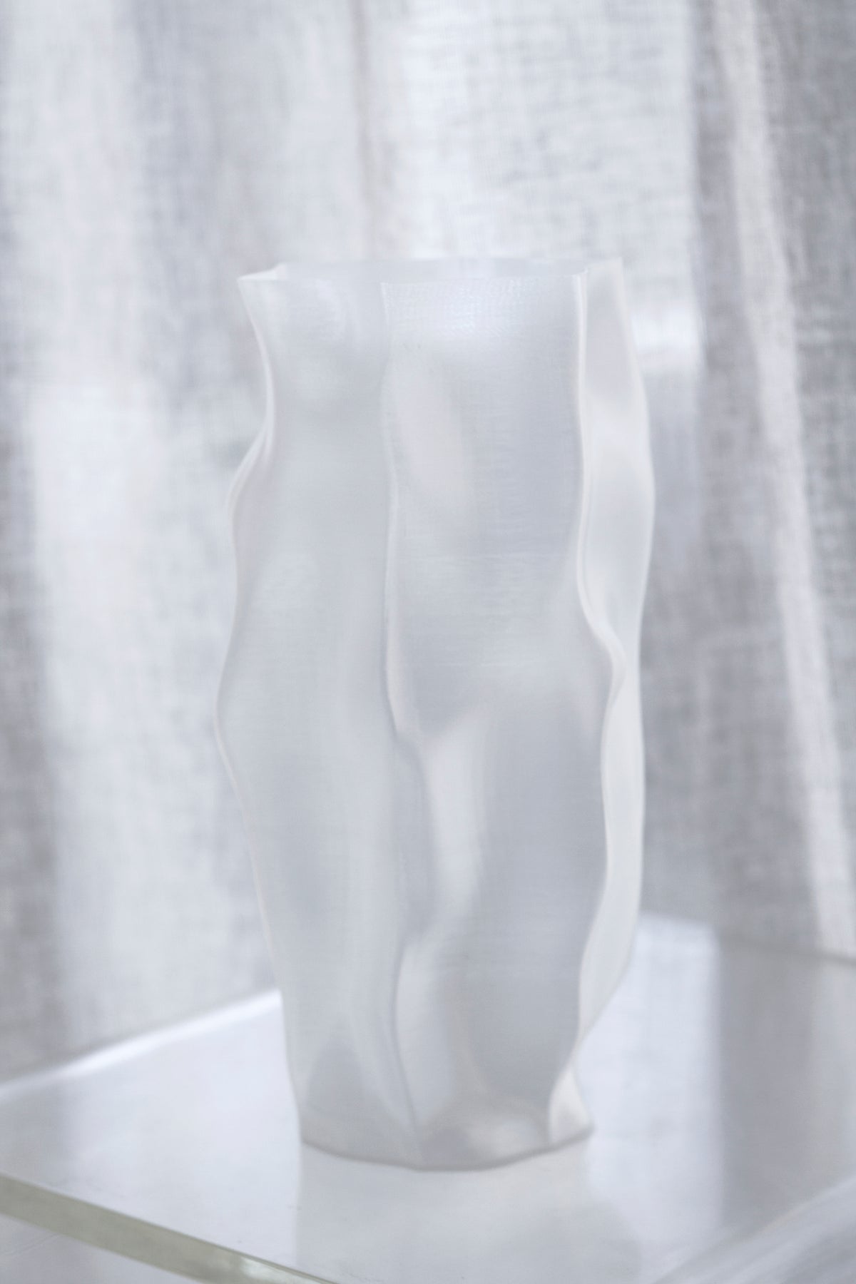 Ripple vase on a pale ledge, linen curtain drawn across the window behind it