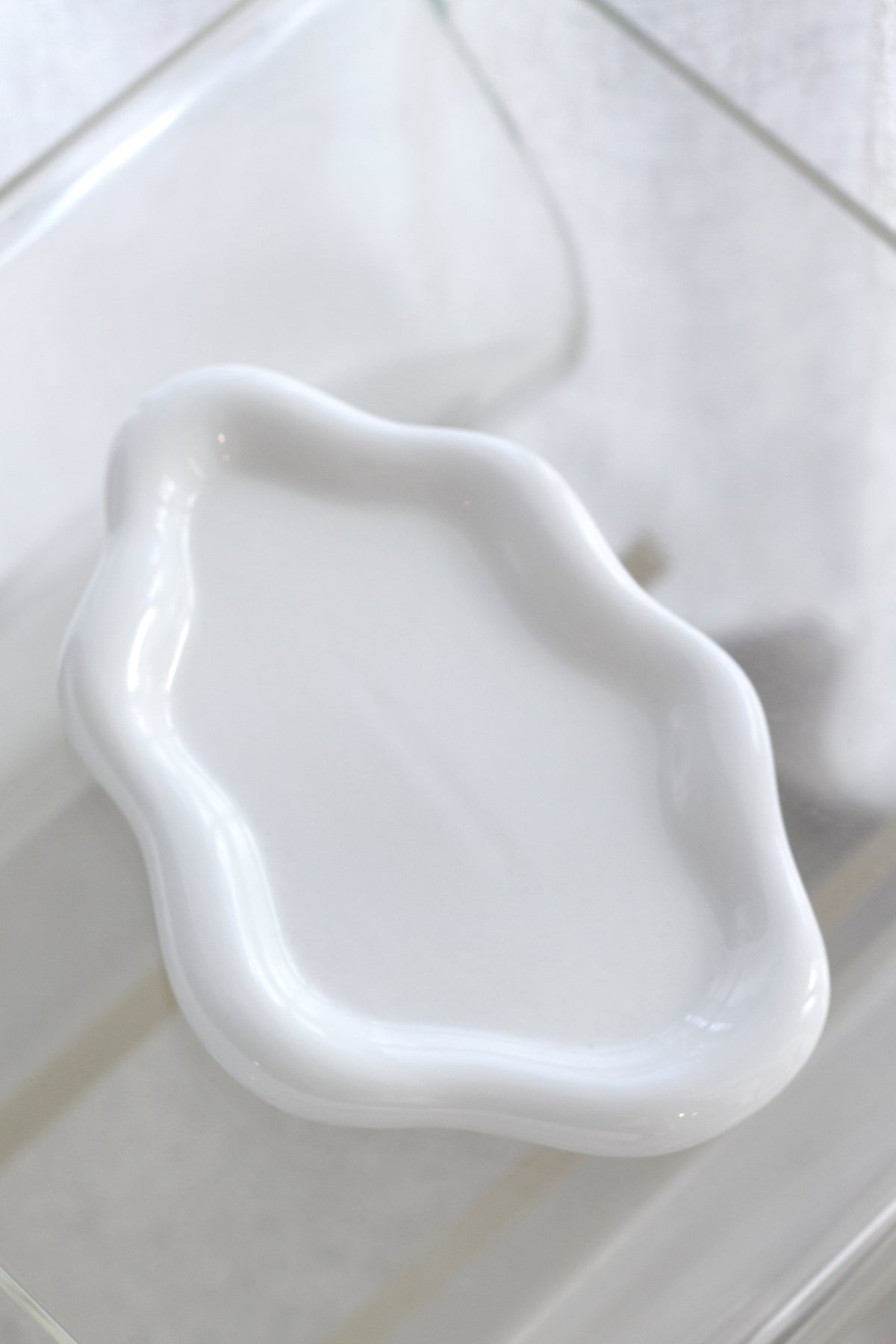 Empty glossy white cloud ceramic tray seen at an angle on a clear surface