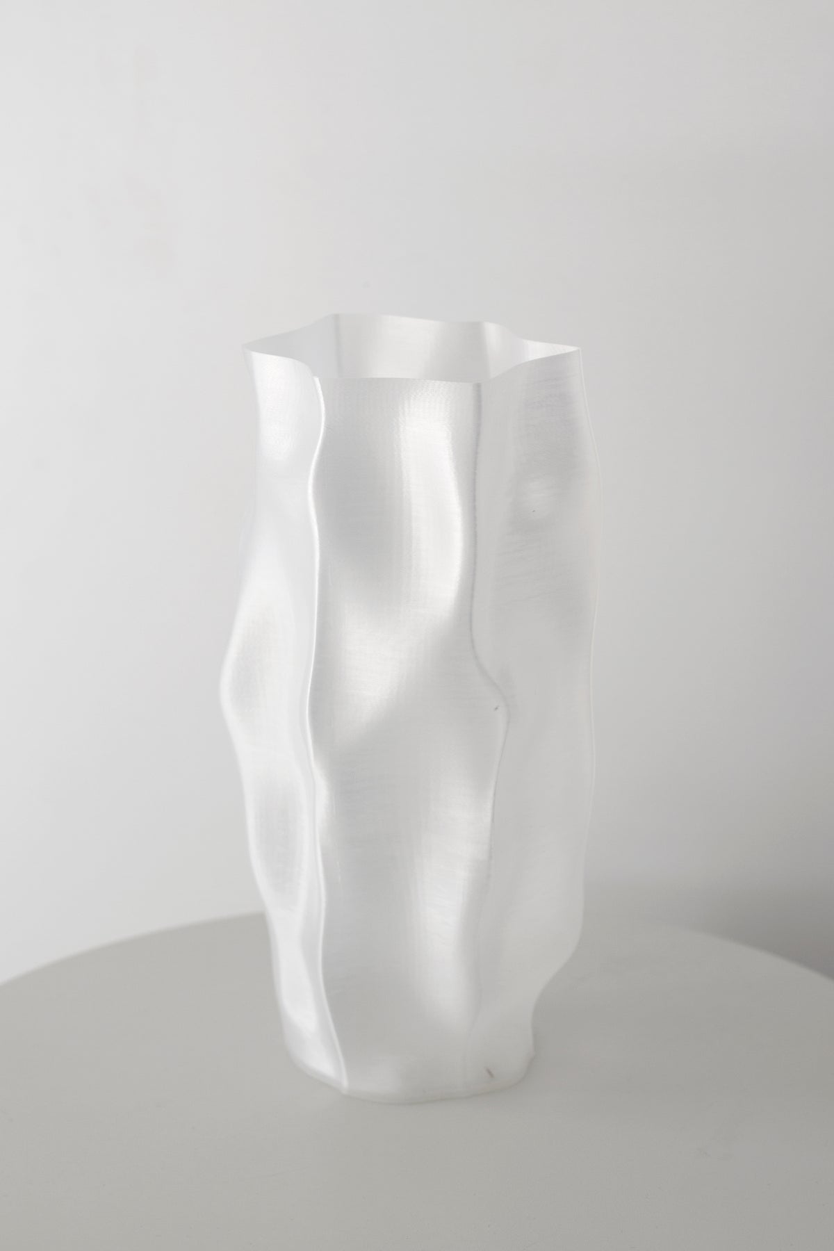 Transparent white ripple vase standing alone on a pale round table against a grey wall