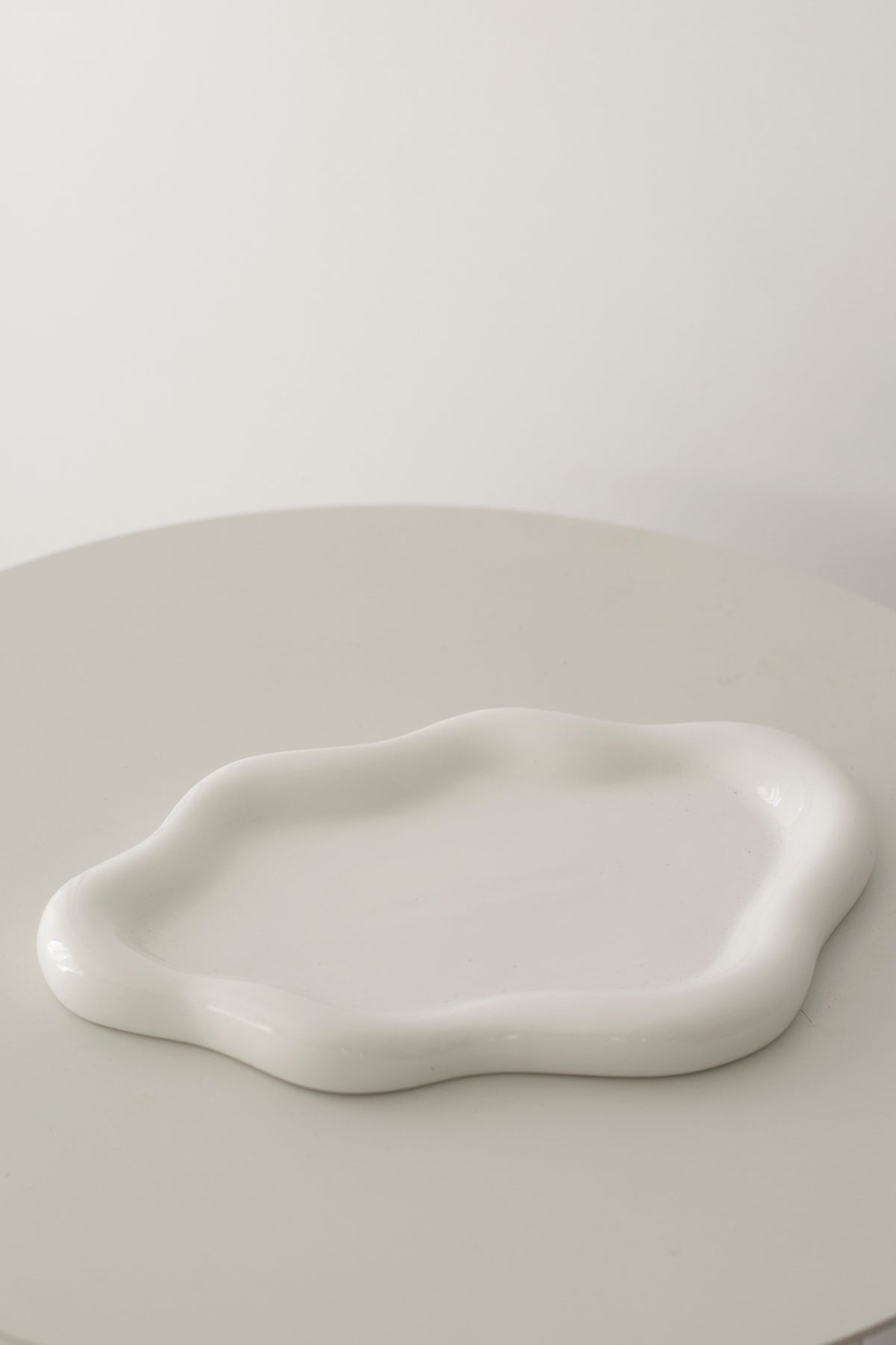Empty white cloud ceramic tray on a round pale table, showing the sculptural wavy rim