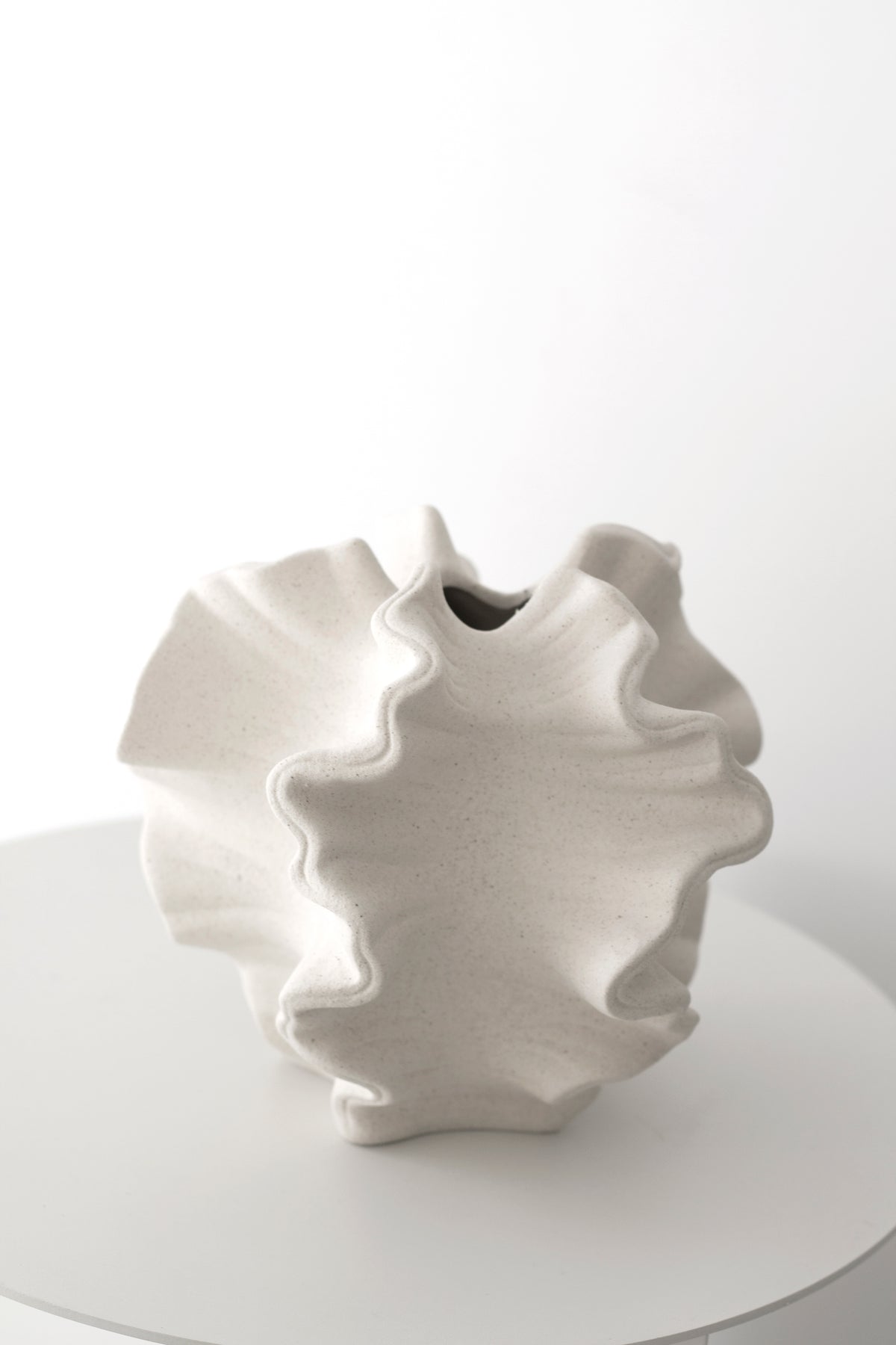 Coral vase alone on a round white pedestal against a plain wall