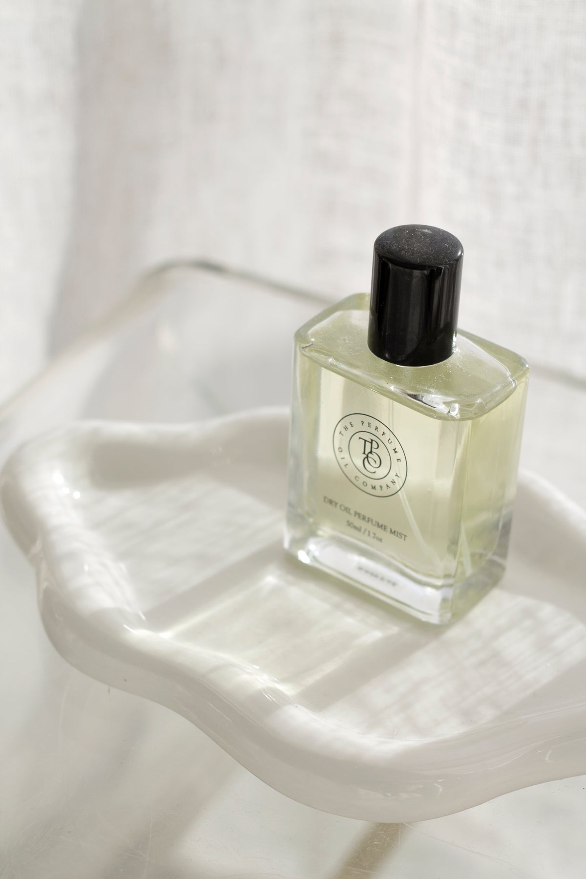 White cloud ceramic tray holding a square perfume bottle on a clear surface