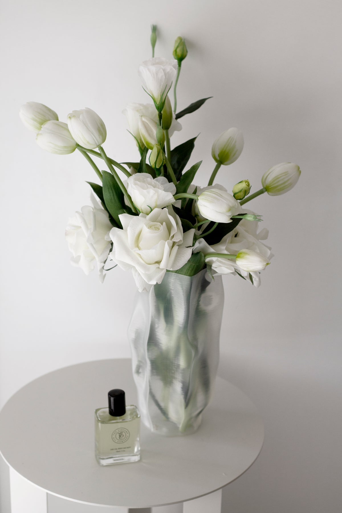 Tulips and roses in the ripple vase on a round white table with a perfume bottle alongside