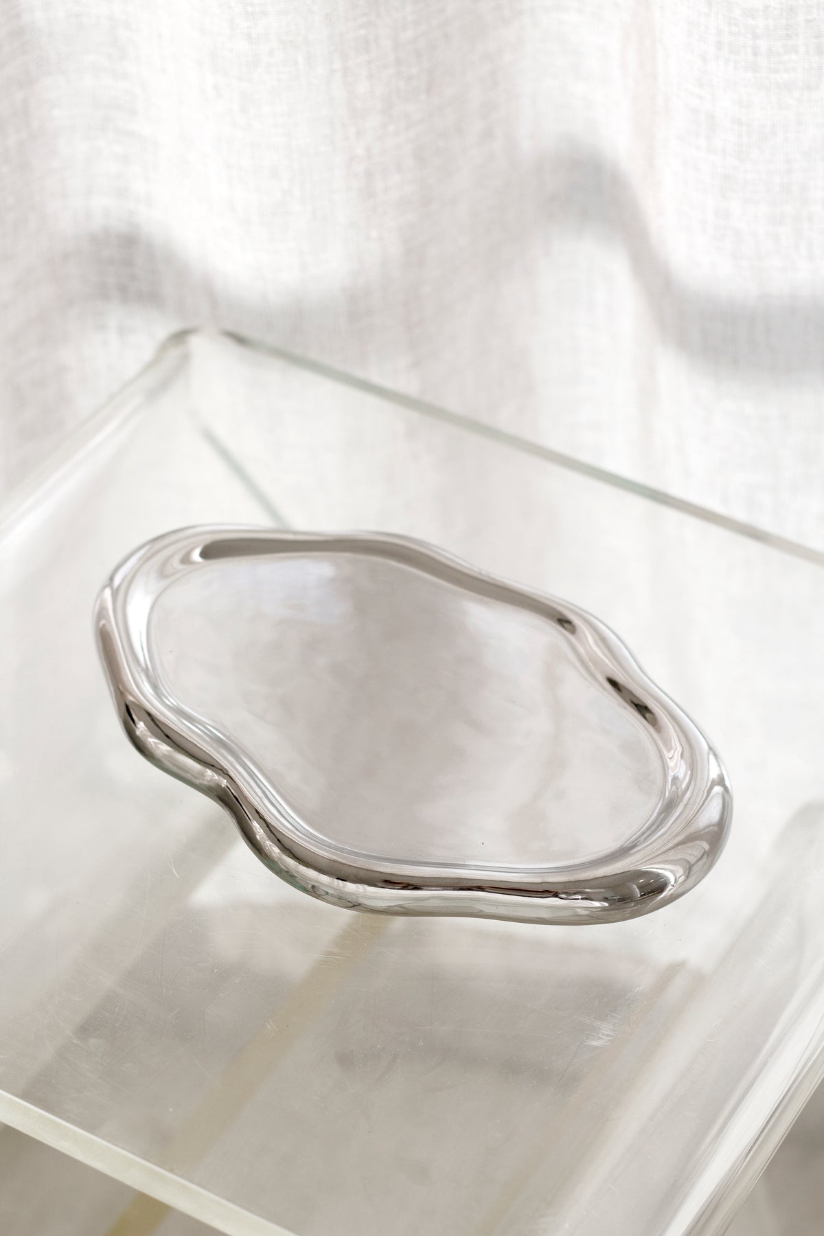 Empty silver electroplated cloud tray on a clear acrylic surface, showing its wavy organic outline
