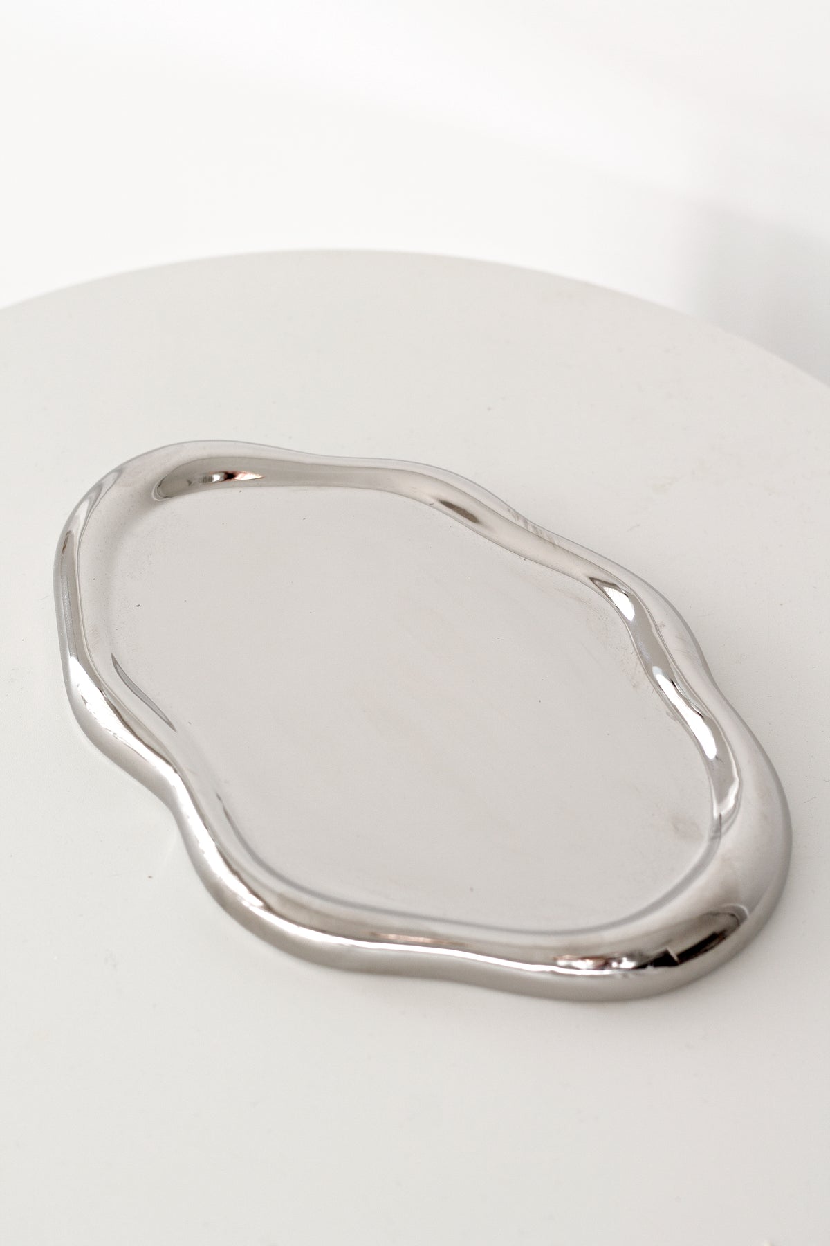 Empty silver electroplated cloud tray on a round white table, showing the mirrored finish and rippled edge