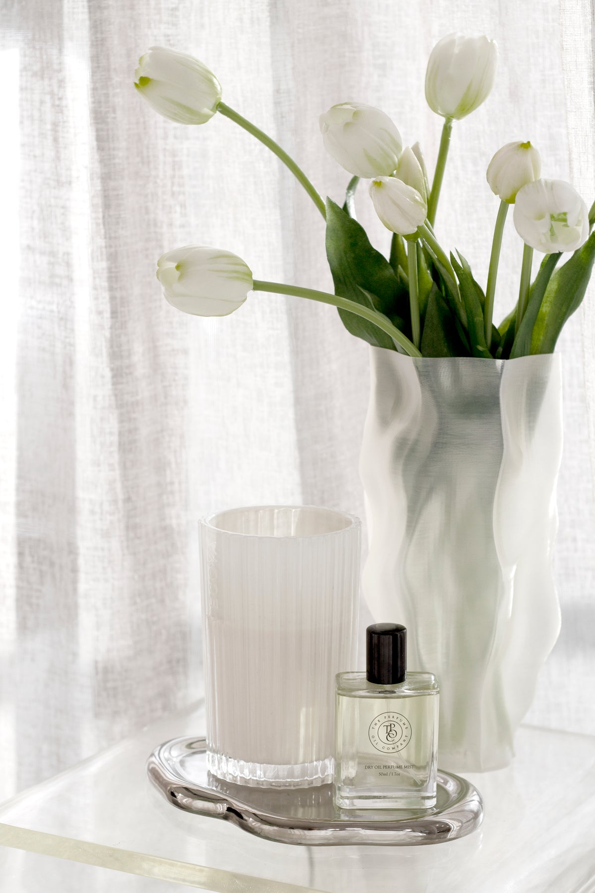 Tulips in the ripple vase beside a fluted candle and a perfume bottle on a silver tray