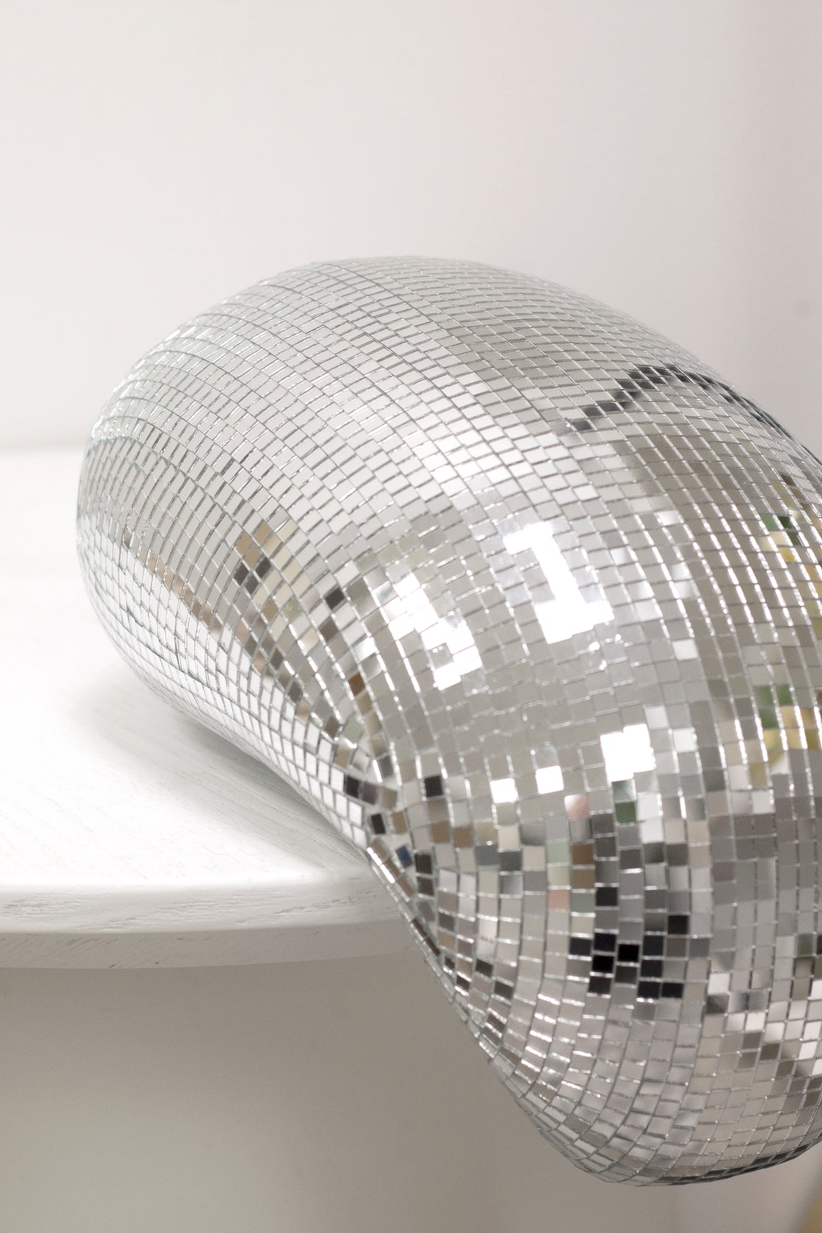 Melting disco ball on a pale ledge, seen from the side
