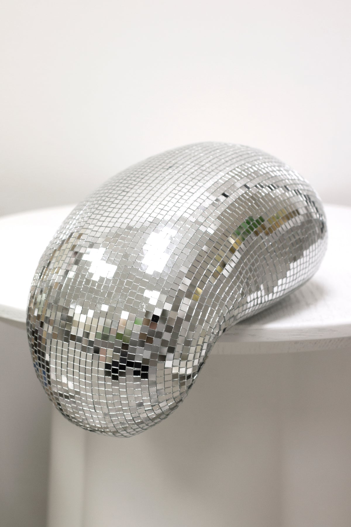 Melting disco ball on a round white pedestal in soft daylight