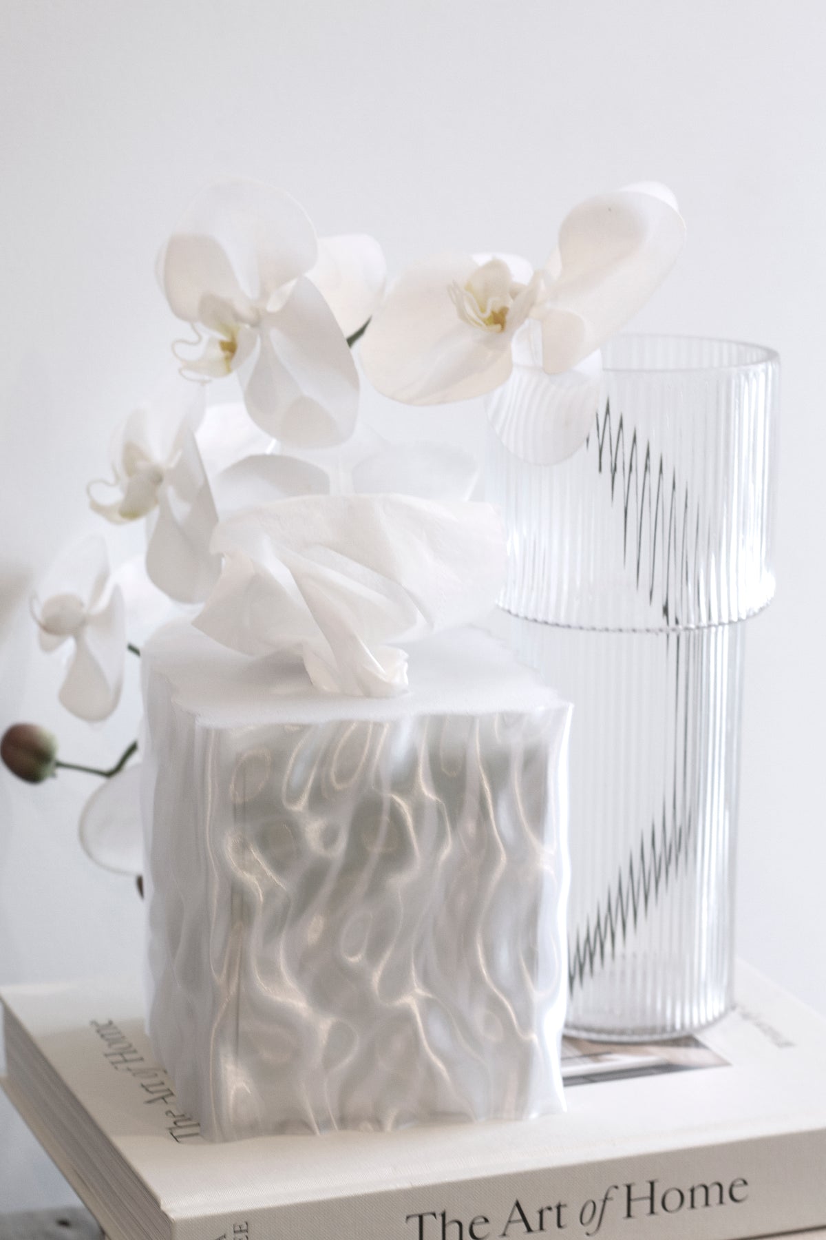 White Flow tissue box cover beside white orchids in a ribbed glass vase on a book