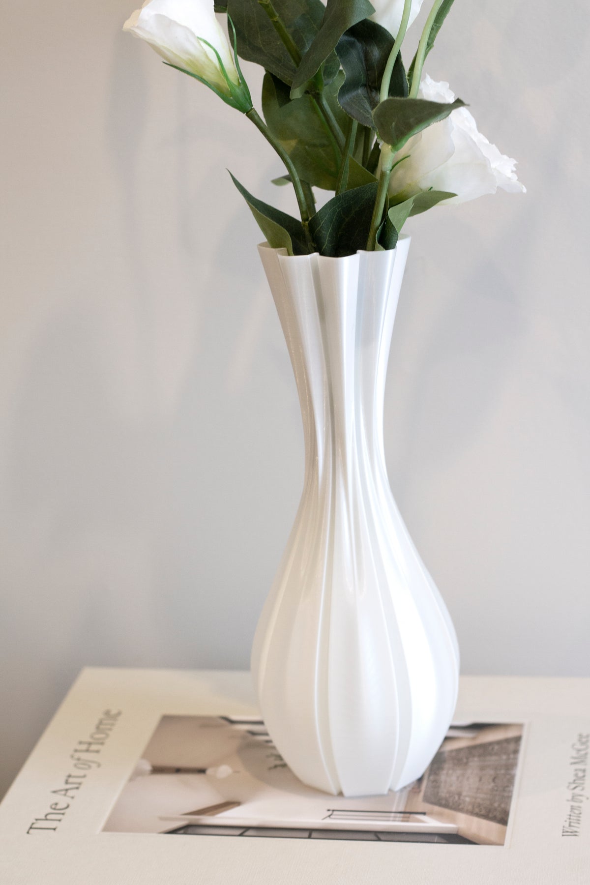 Fluted white vase of lisianthus standing on an open book, the ribbed body lit from the side