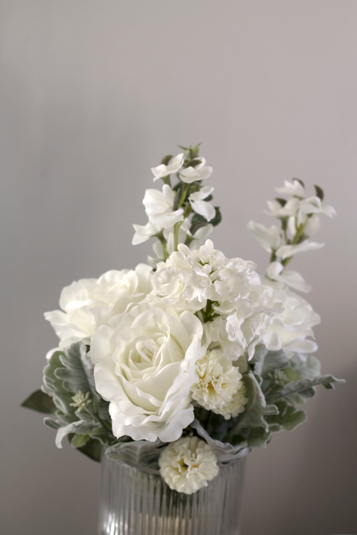 White faux roses and sweet peas against a warm grey background