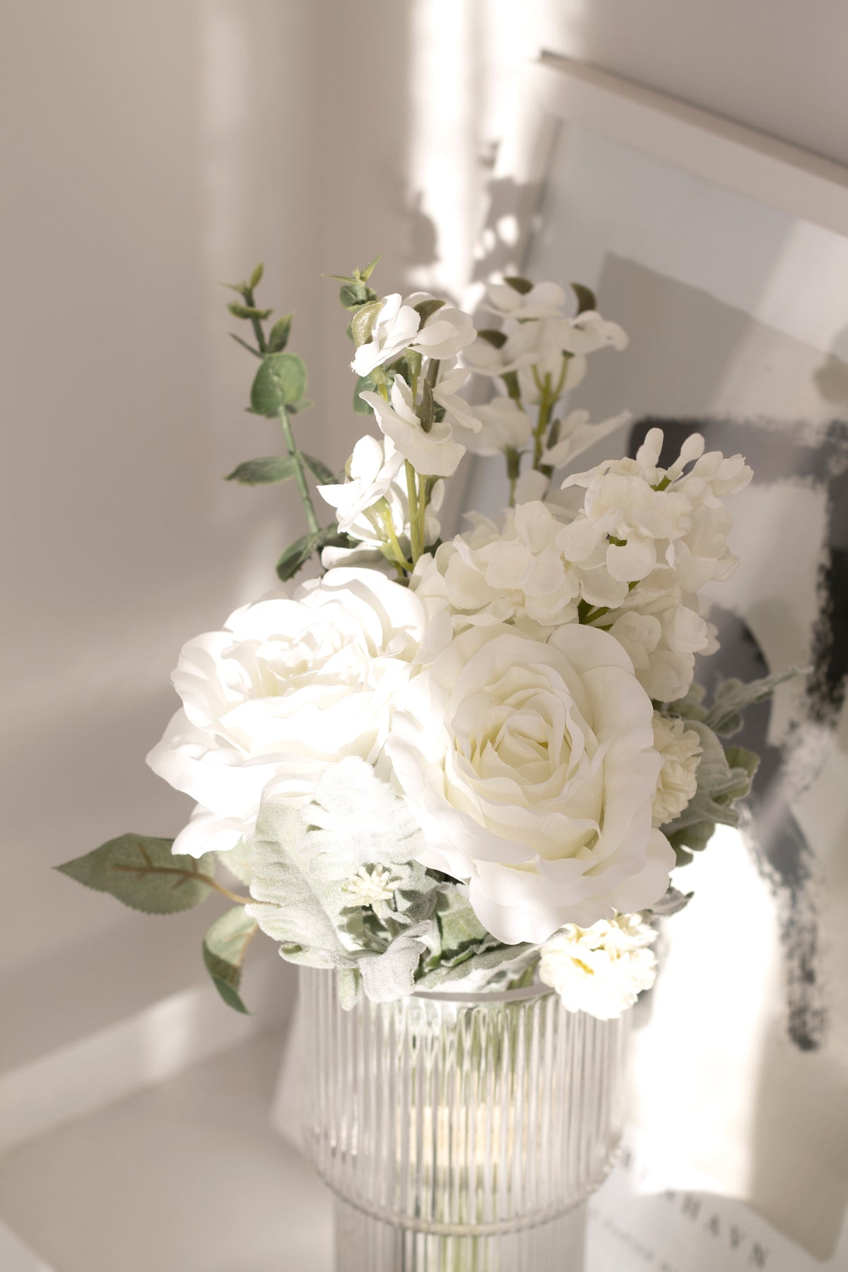 White faux bouquet with eucalyptus in a ribbed glass vase