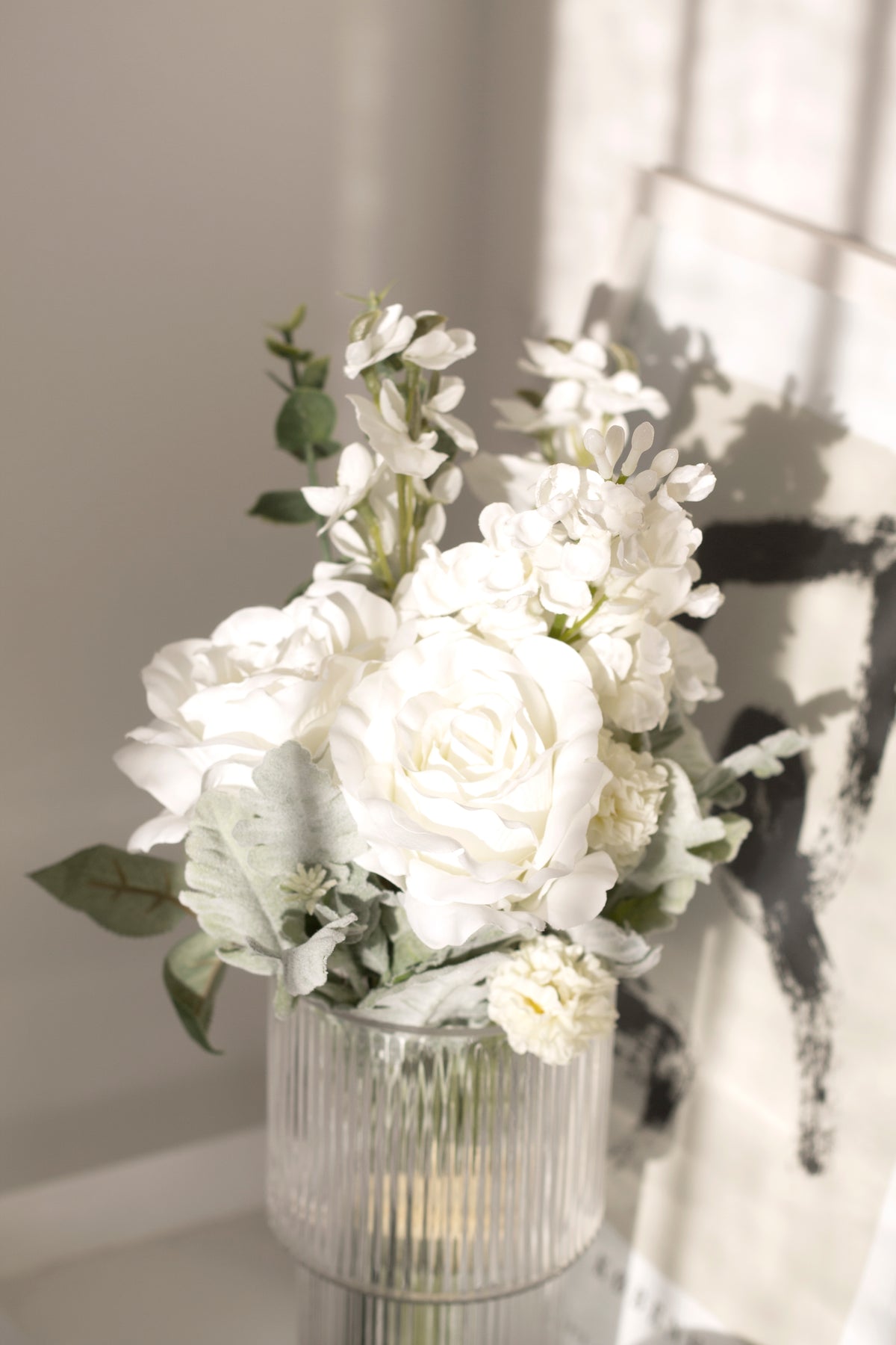 Close view of white faux roses in a ribbed glass vase