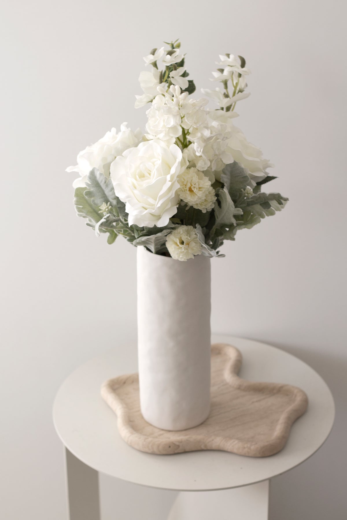 White faux bouquet in a tall white vase on a round side table