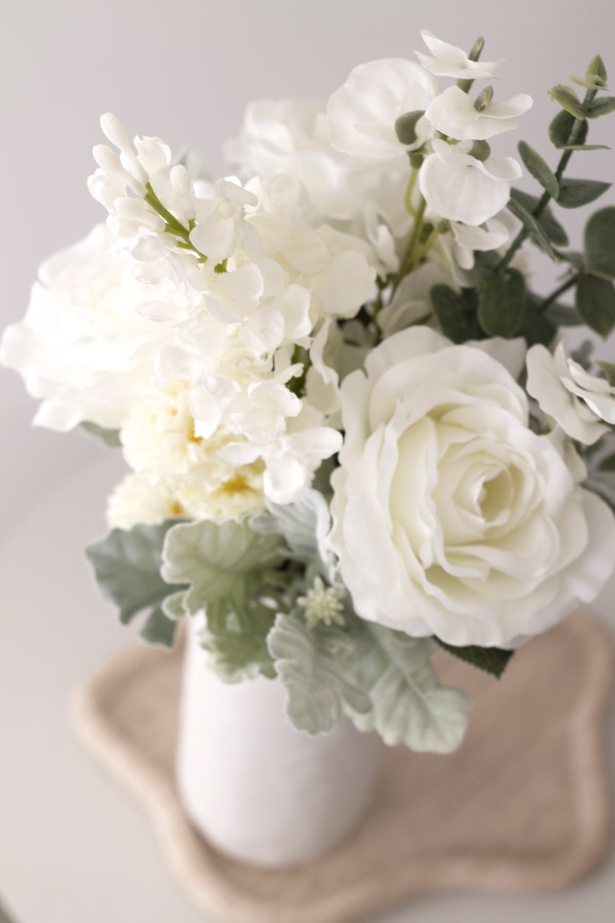 White faux bouquet with green foliage in a white swirl vase