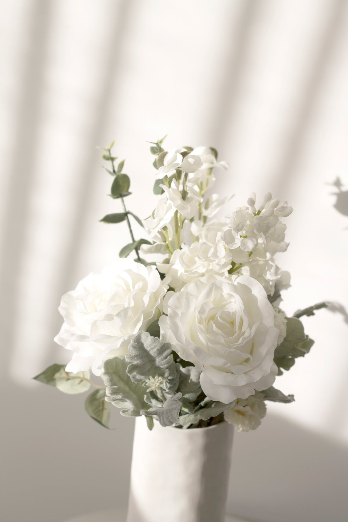 White faux bouquet in a slim vase against sheer curtains