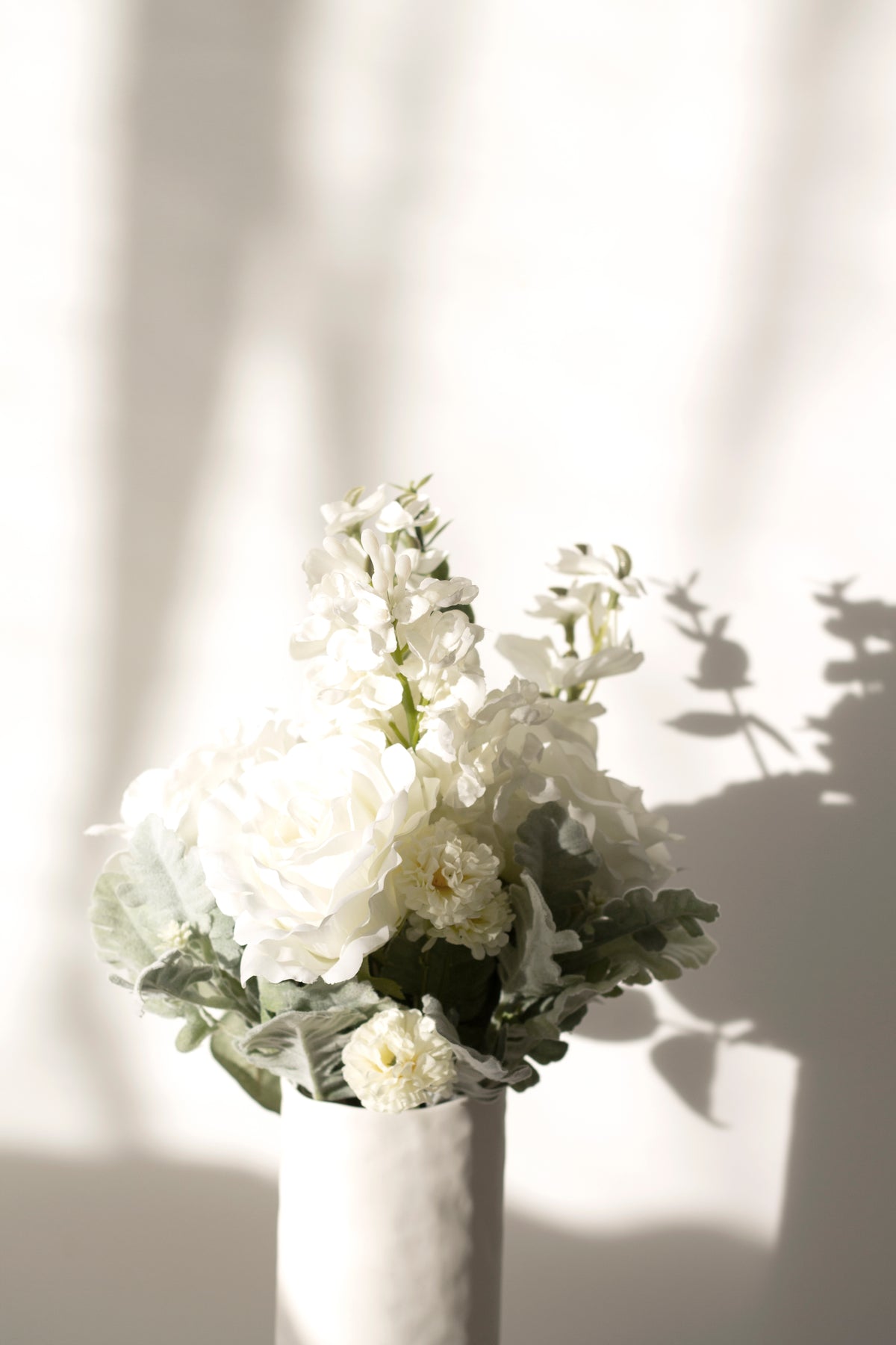 White faux bouquet in a slim glass vase in window light