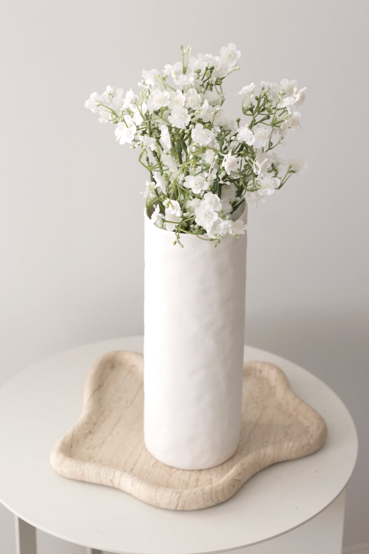 Faux gypsophila in a tall white vase on a timber stool