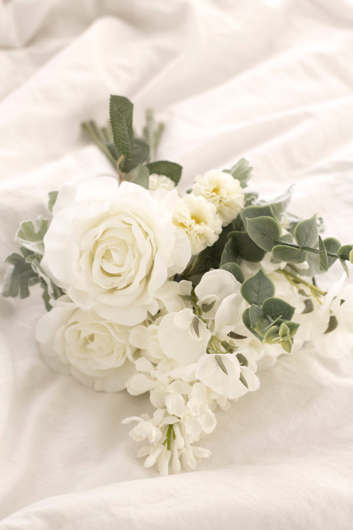 Close view of white faux roses and sweet peas on soft linen