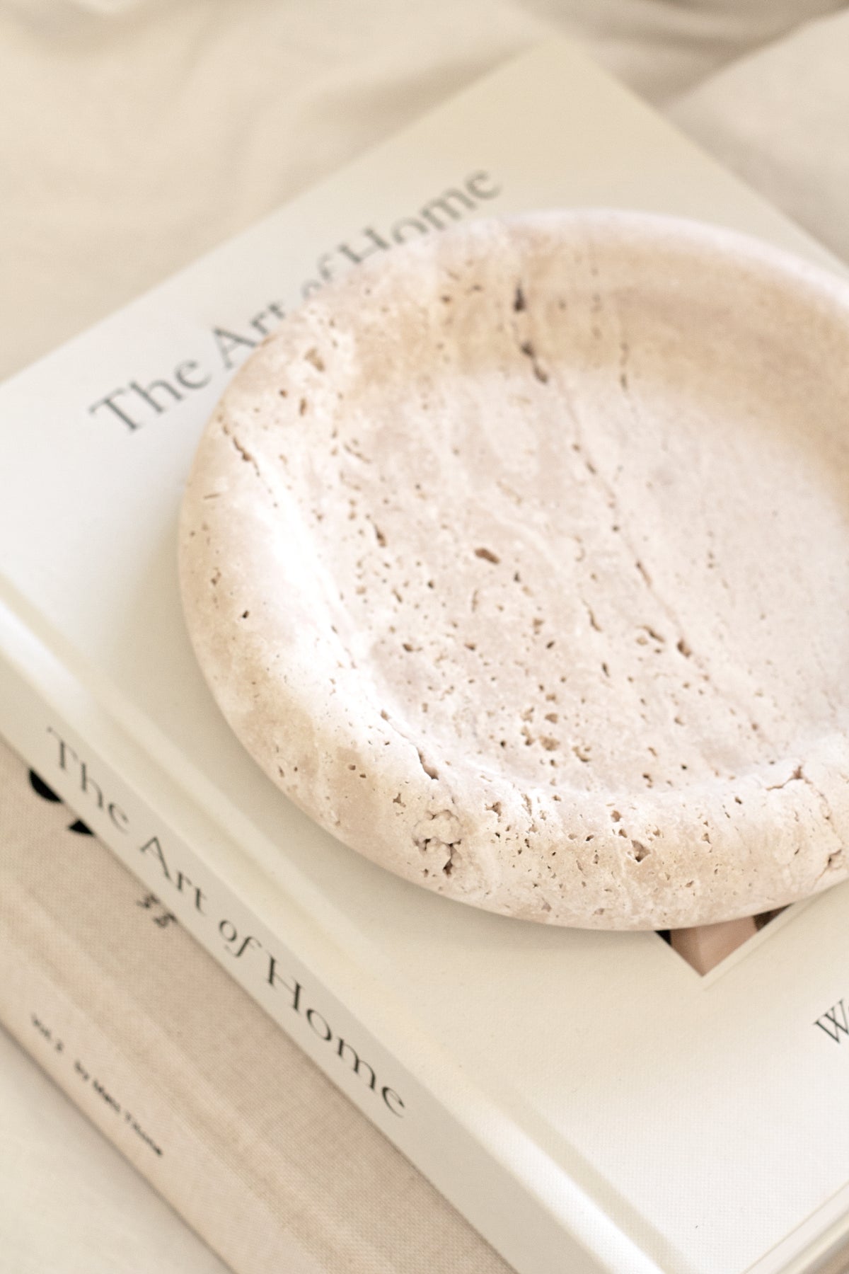 Close-up of the Bay Round Tray in light travertine resting on a coffee table book