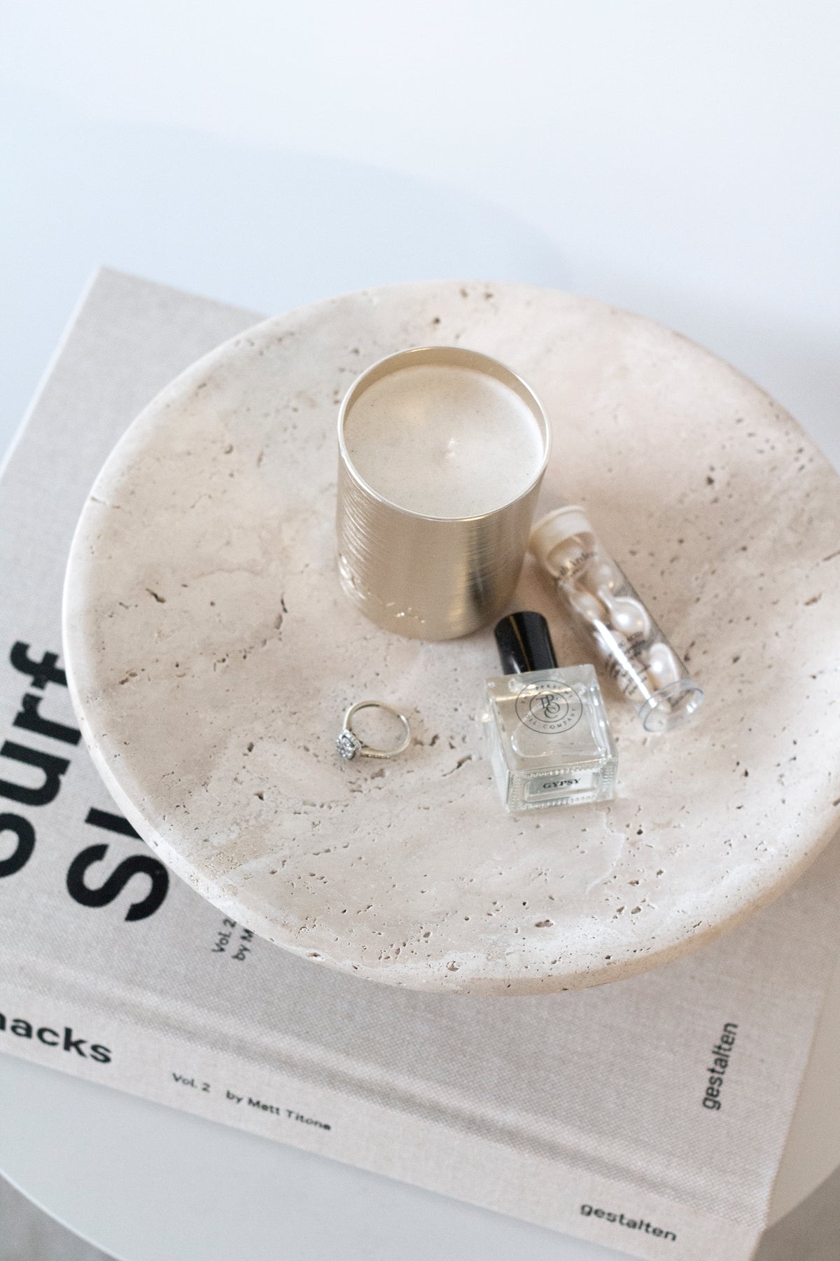 Candle, glass perfume bottle and rings arranged on a Nome stand resting on a book