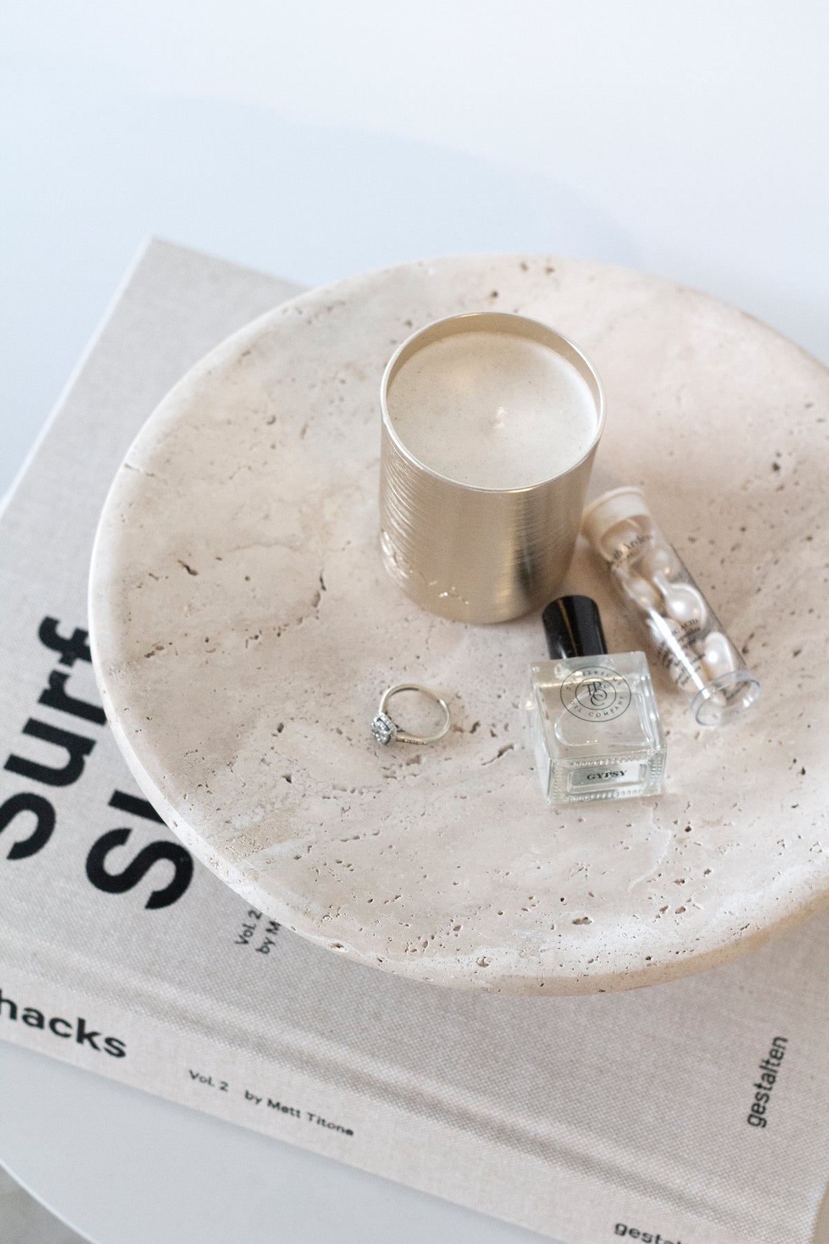 Nome stand holding a candle, a perfume bottle and rings on top of a coffee table book
