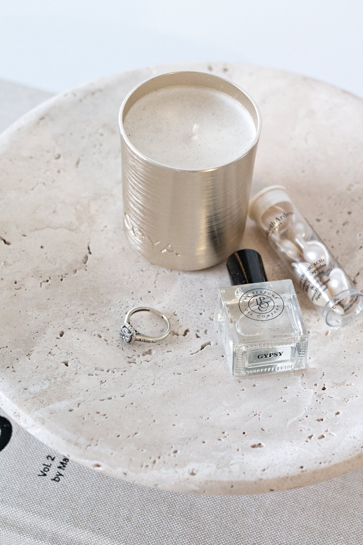 Top-down view of a candle, perfume and rings on the pitted surface of a Nome travertine stand