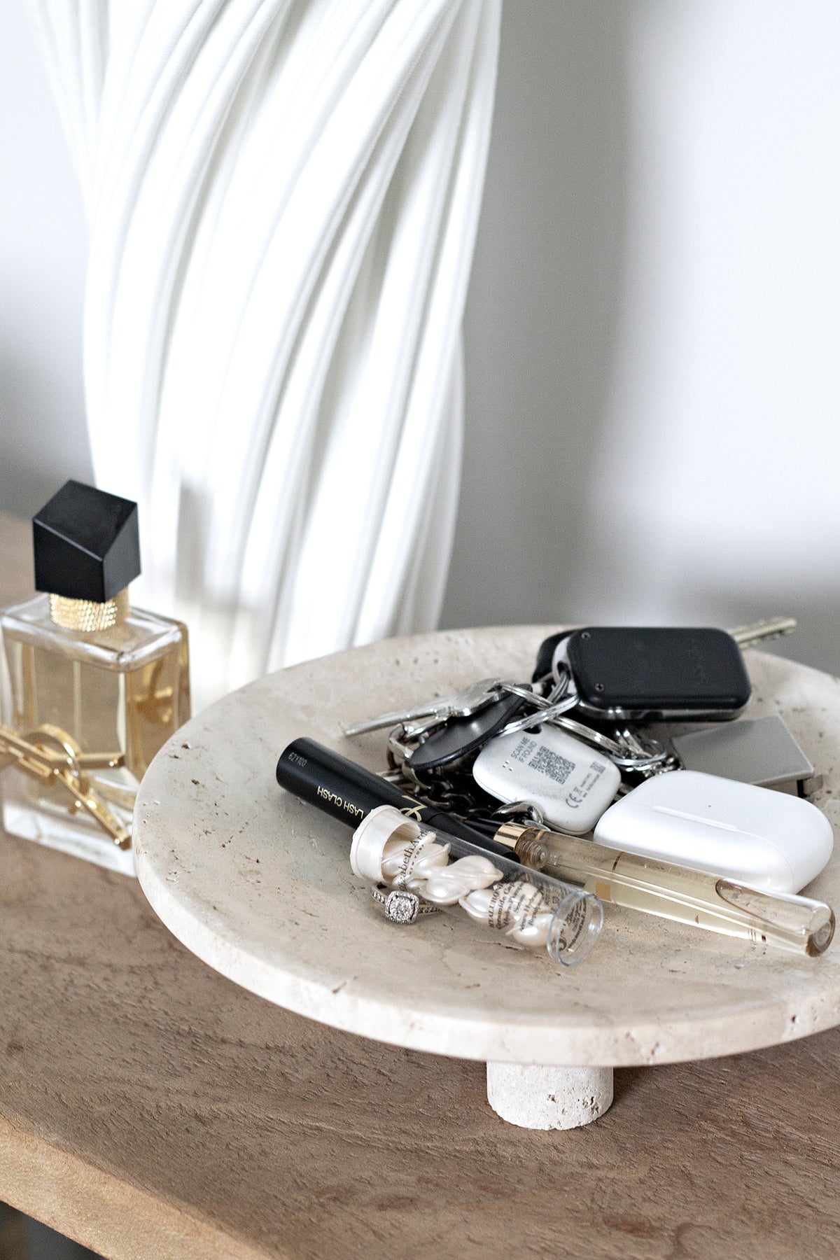 Close view of a Nome stand holding keys, perfume and a pearl bracelet on a timber console