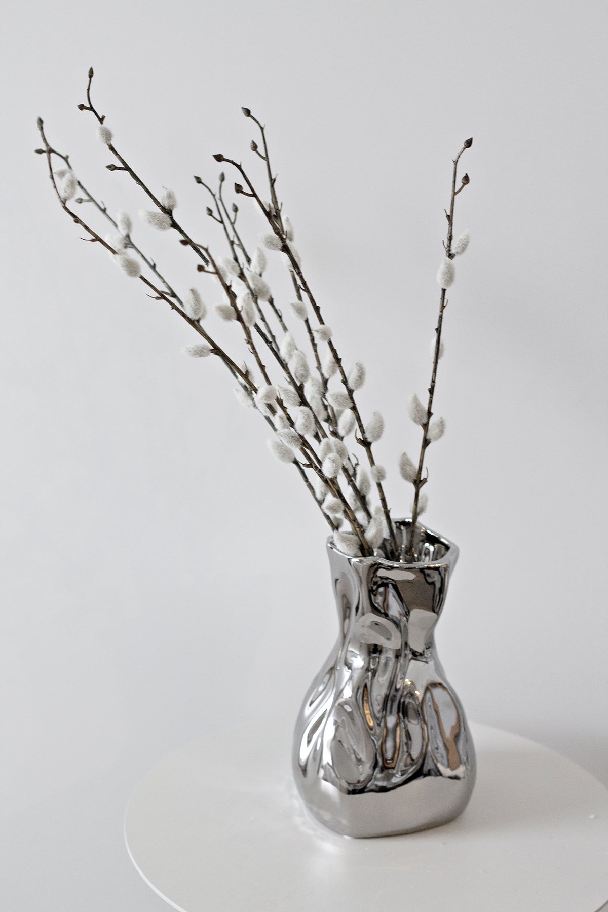 Faux pussy willow stems in a crumpled silver vase
