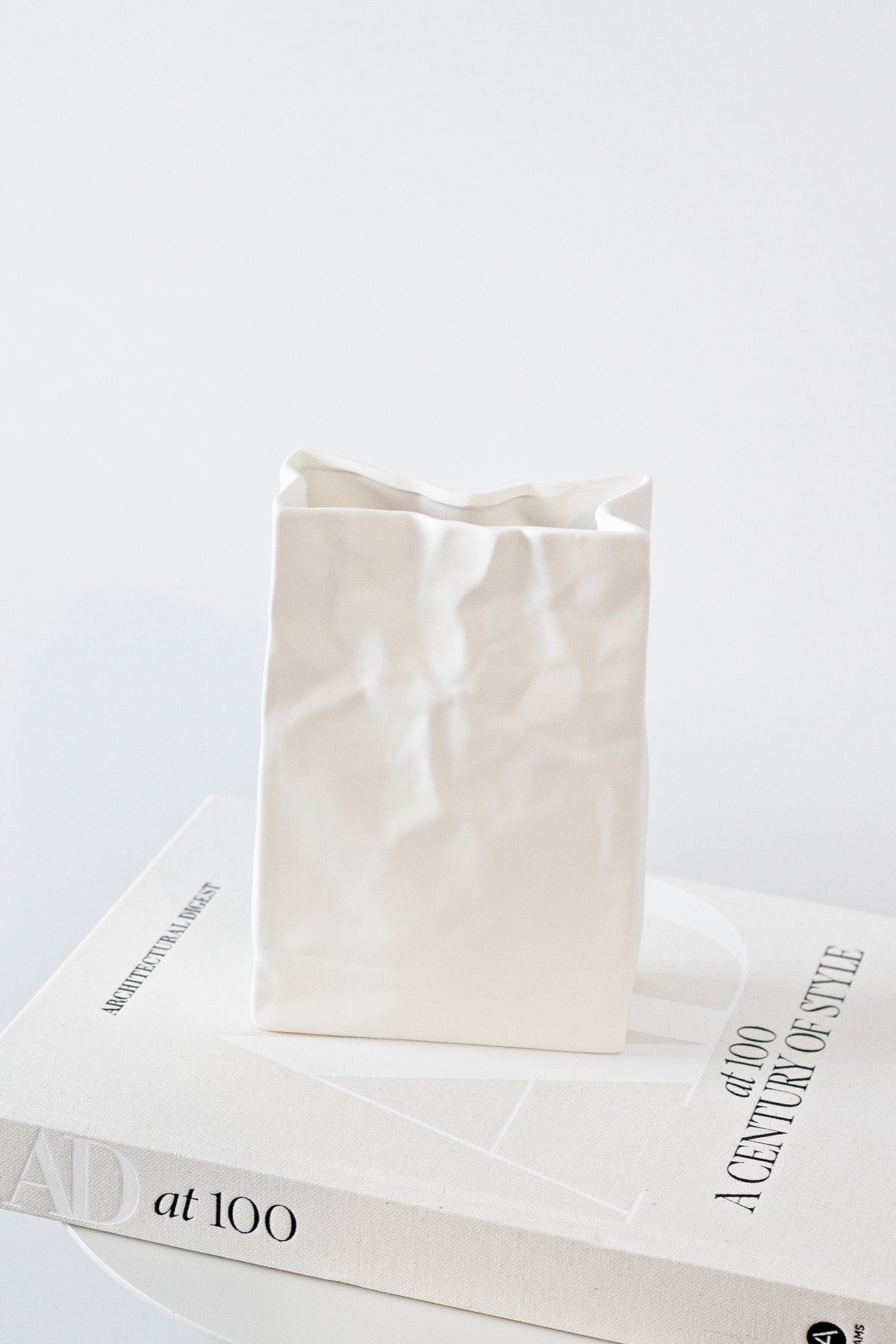 Medium white paper bag vase resting on stacked books against a soft grey background