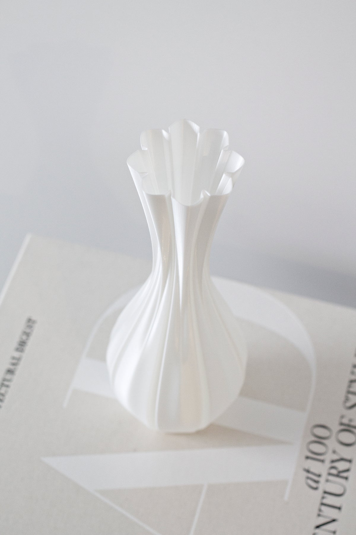 Fluted white vase seen at an angle on a stack of pale books, scalloped rim in focus