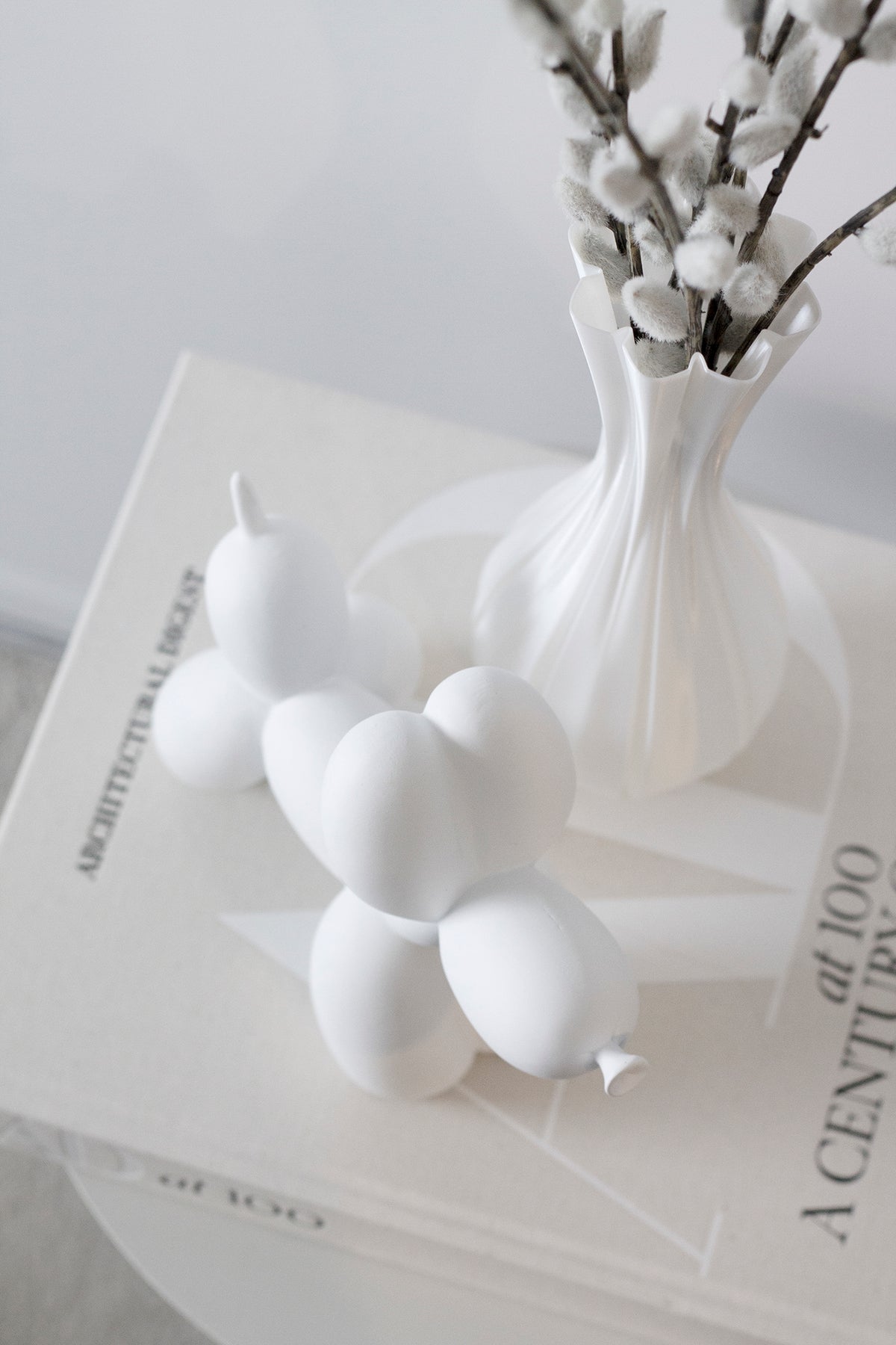 White ceramic balloon dog sculpture beside a vase of white blossom on stacked books