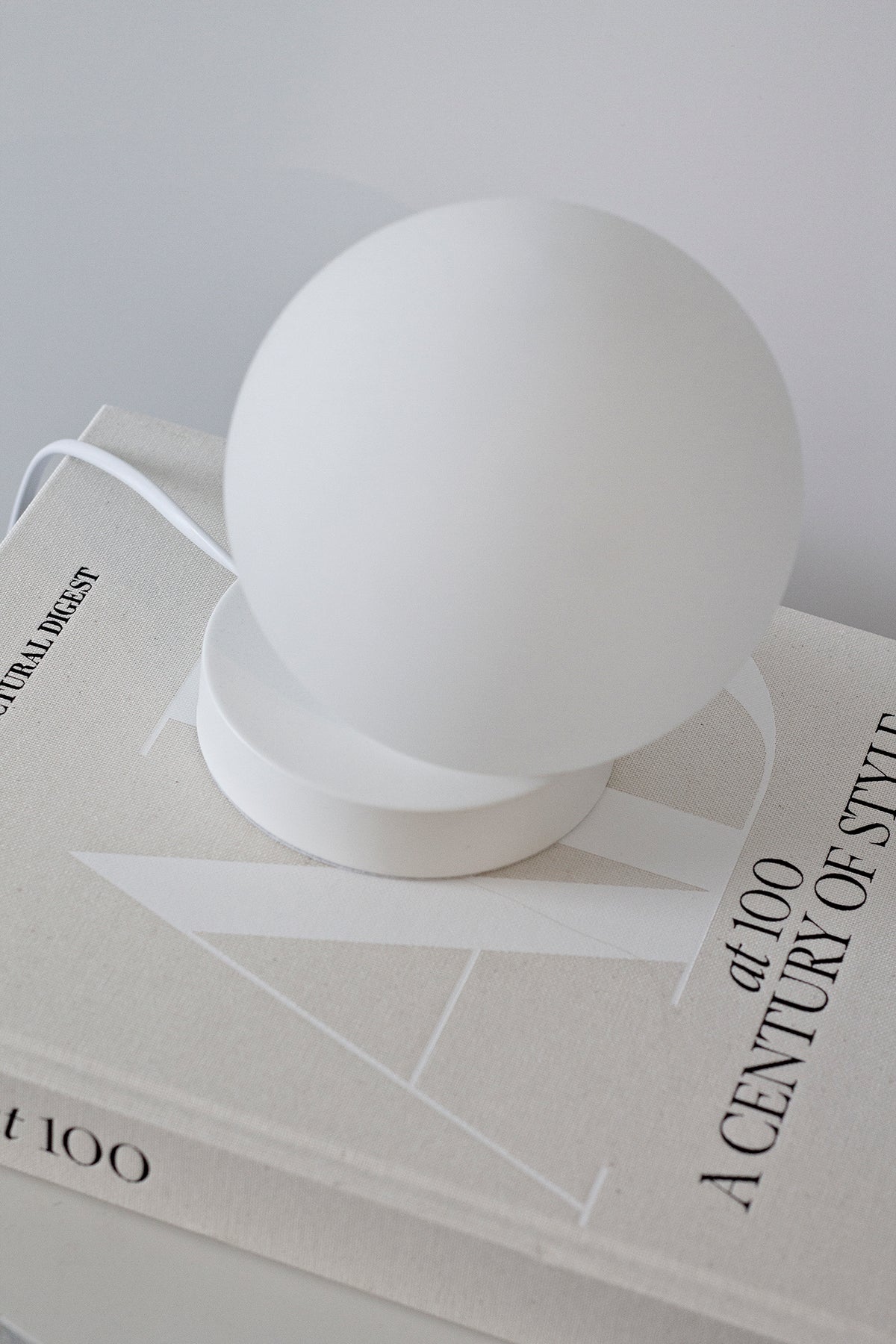 Yuri Table Lamp on white coffee table books, cord trailing behind