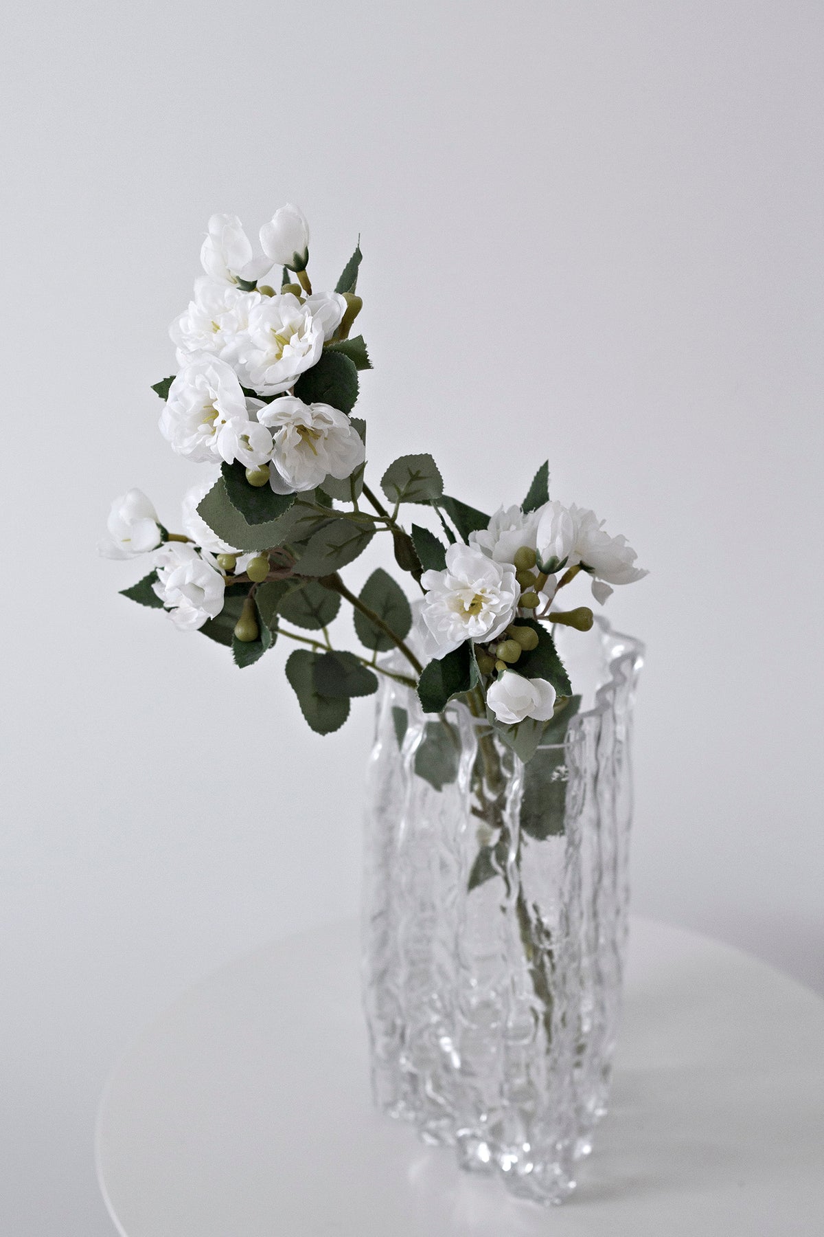 Clear Glacier vase of white blossom and eucalyptus on a round white table