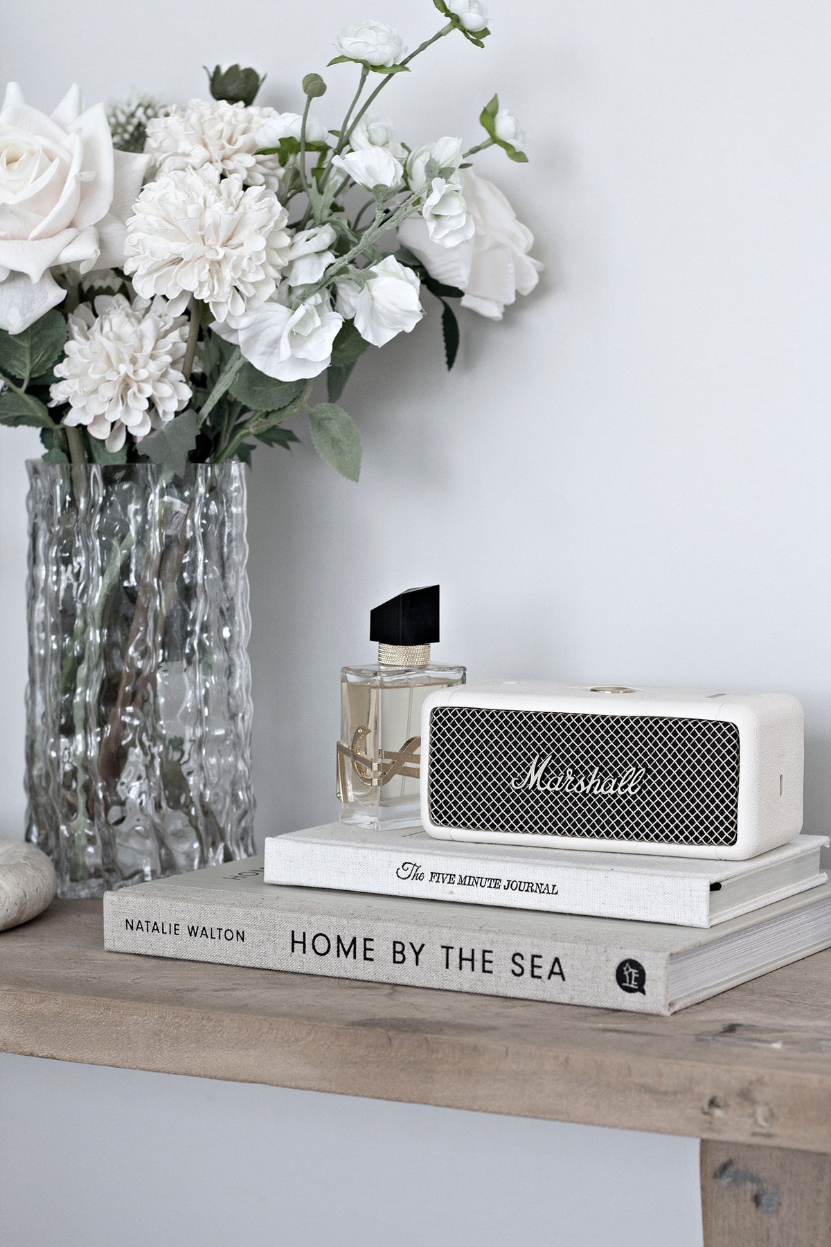 Clear Glacier vase of white carnations on a timber console with books and a speaker