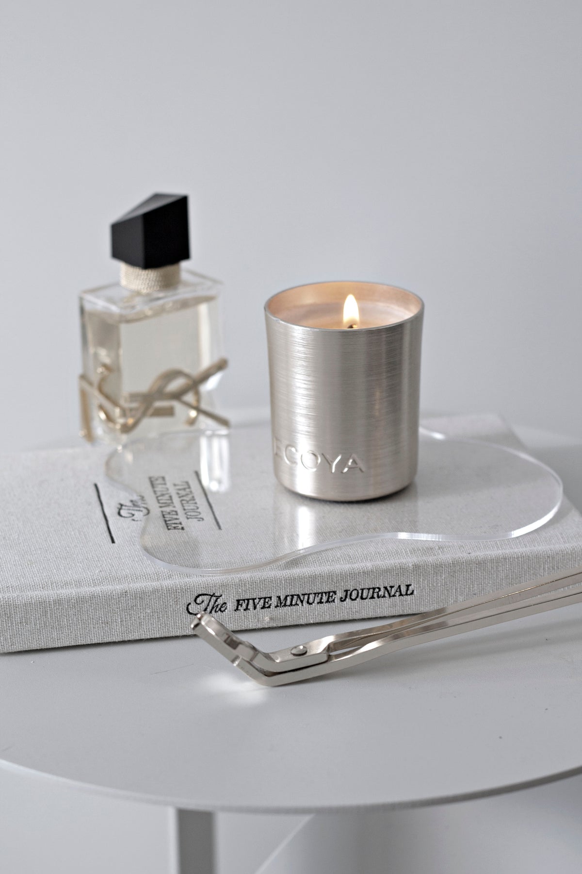 Perfume bottle and a silver candle on the journal atop a round white side table