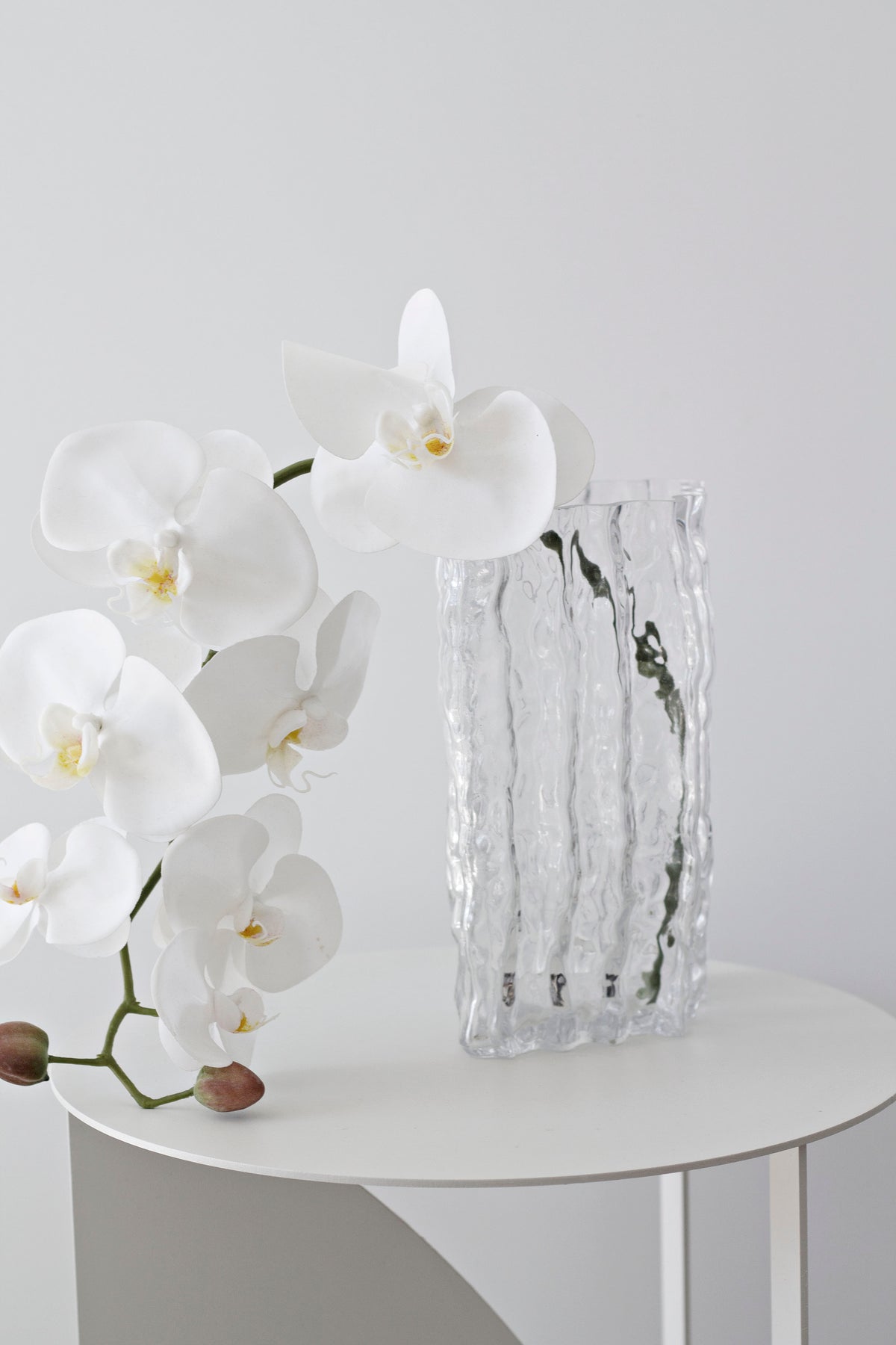 Clear Glacier vase holding white orchids on a round white side table