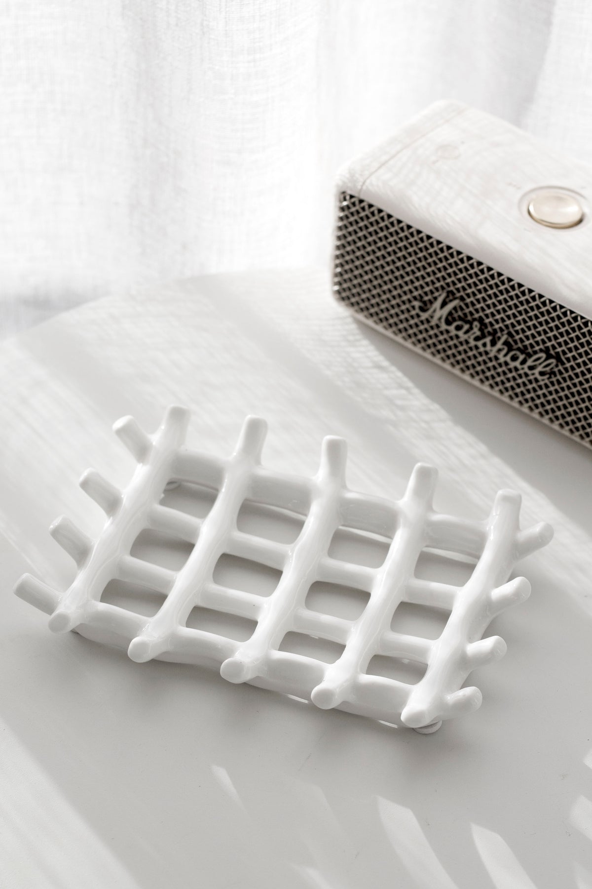 Edie soap dish on a bathroom ledge beside a textured container, curtain behind
