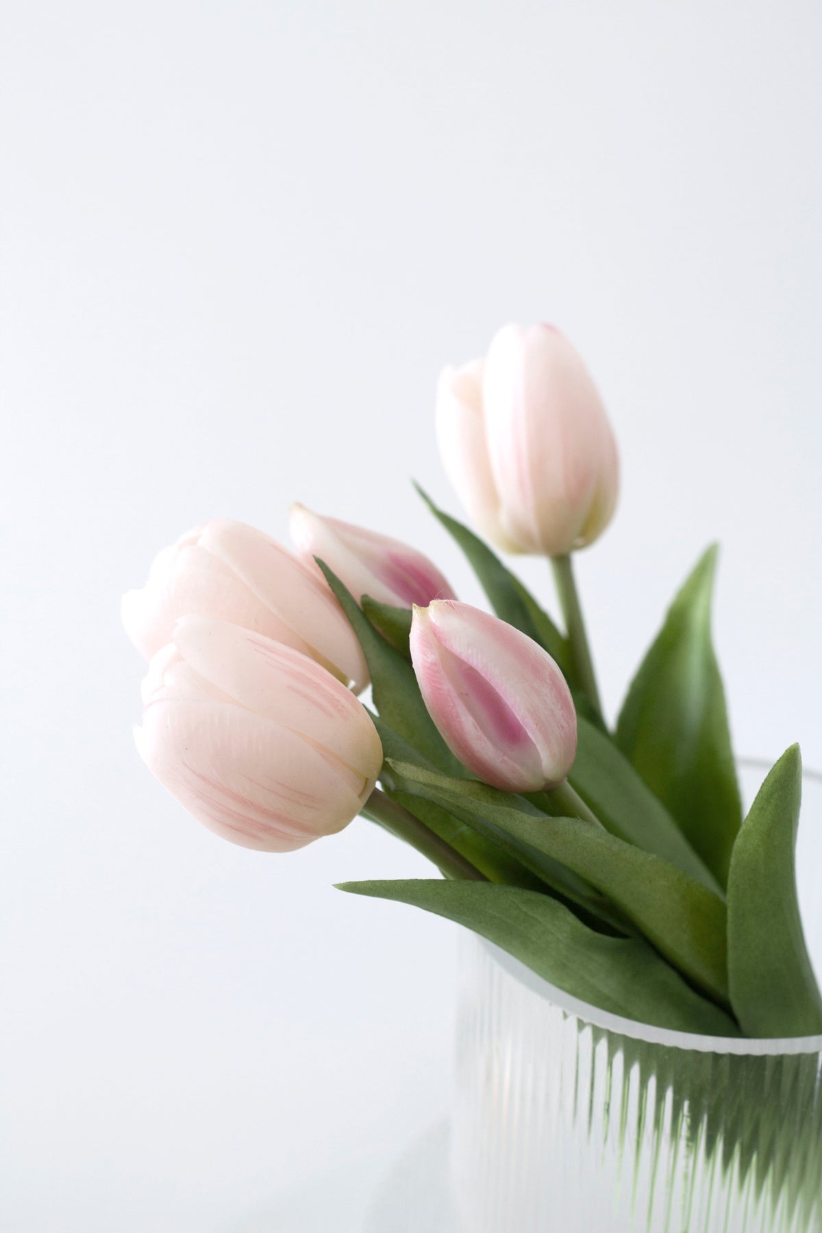Close up of pale pink faux tulips showing the lifelike petals and green foliage