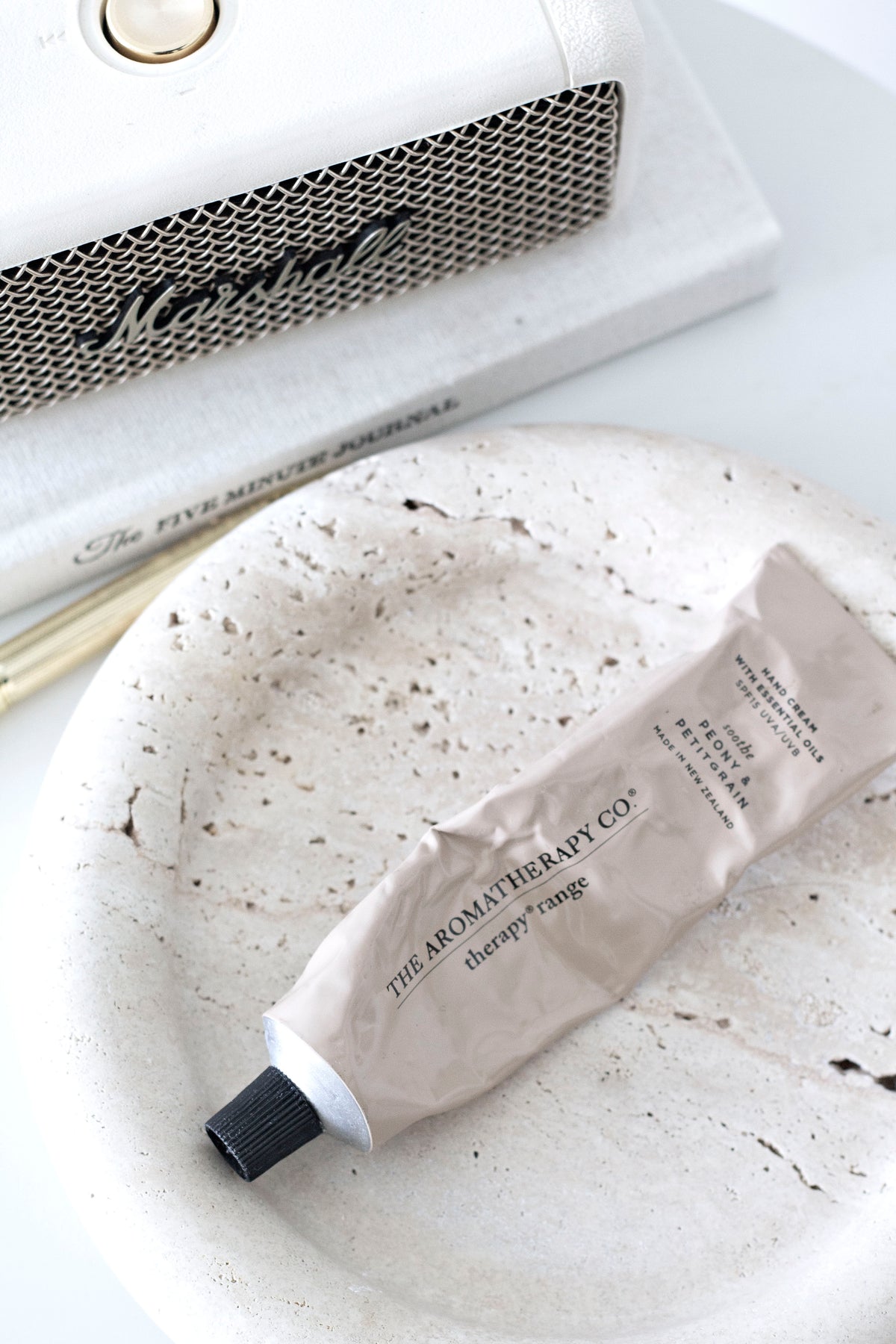 Hand cream tube on a speckled white stone dish beside books and a speaker